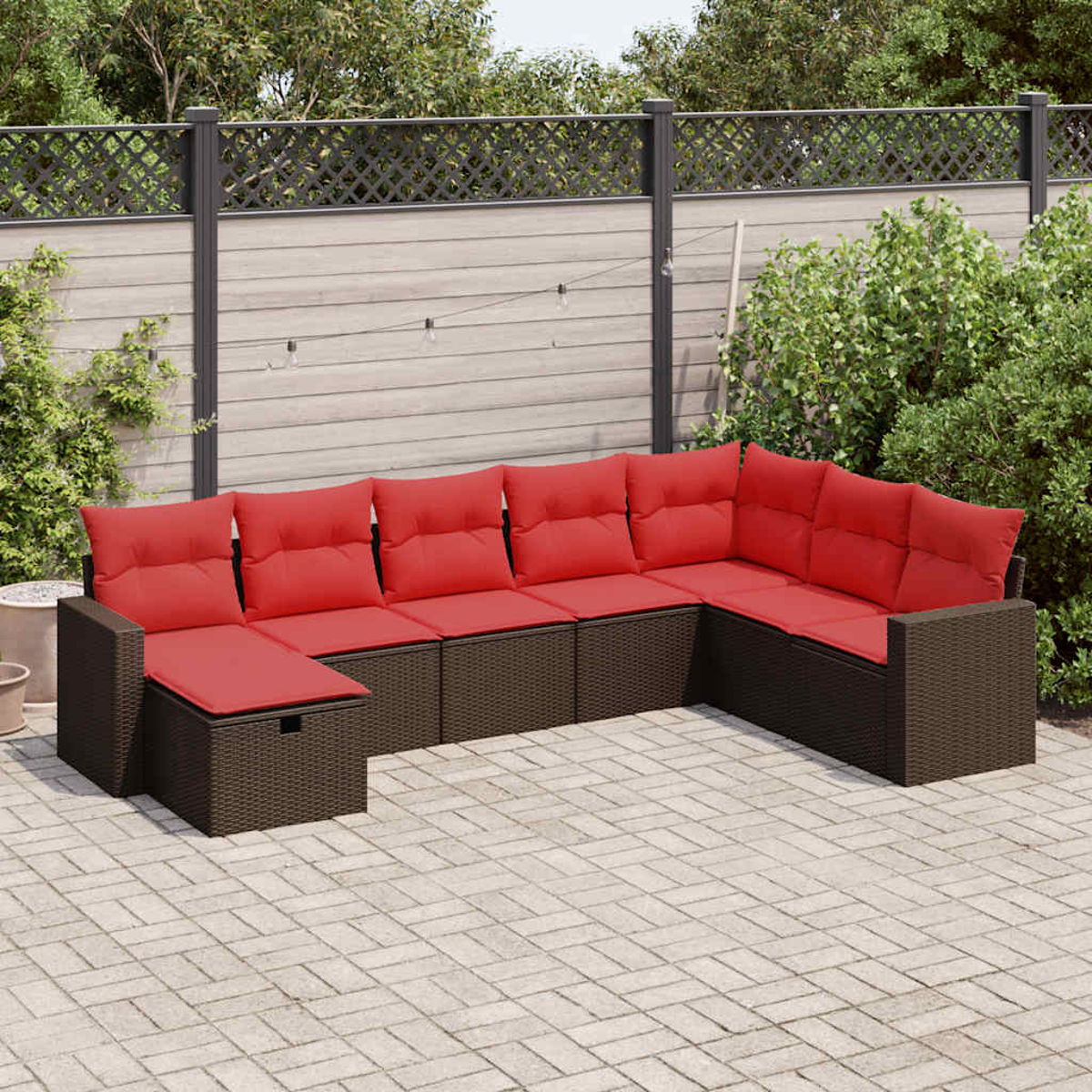 Ein braunes Ecksofa aus Rattan mit roten Kissen im Freien auf einer gepflasterten Terrasse.