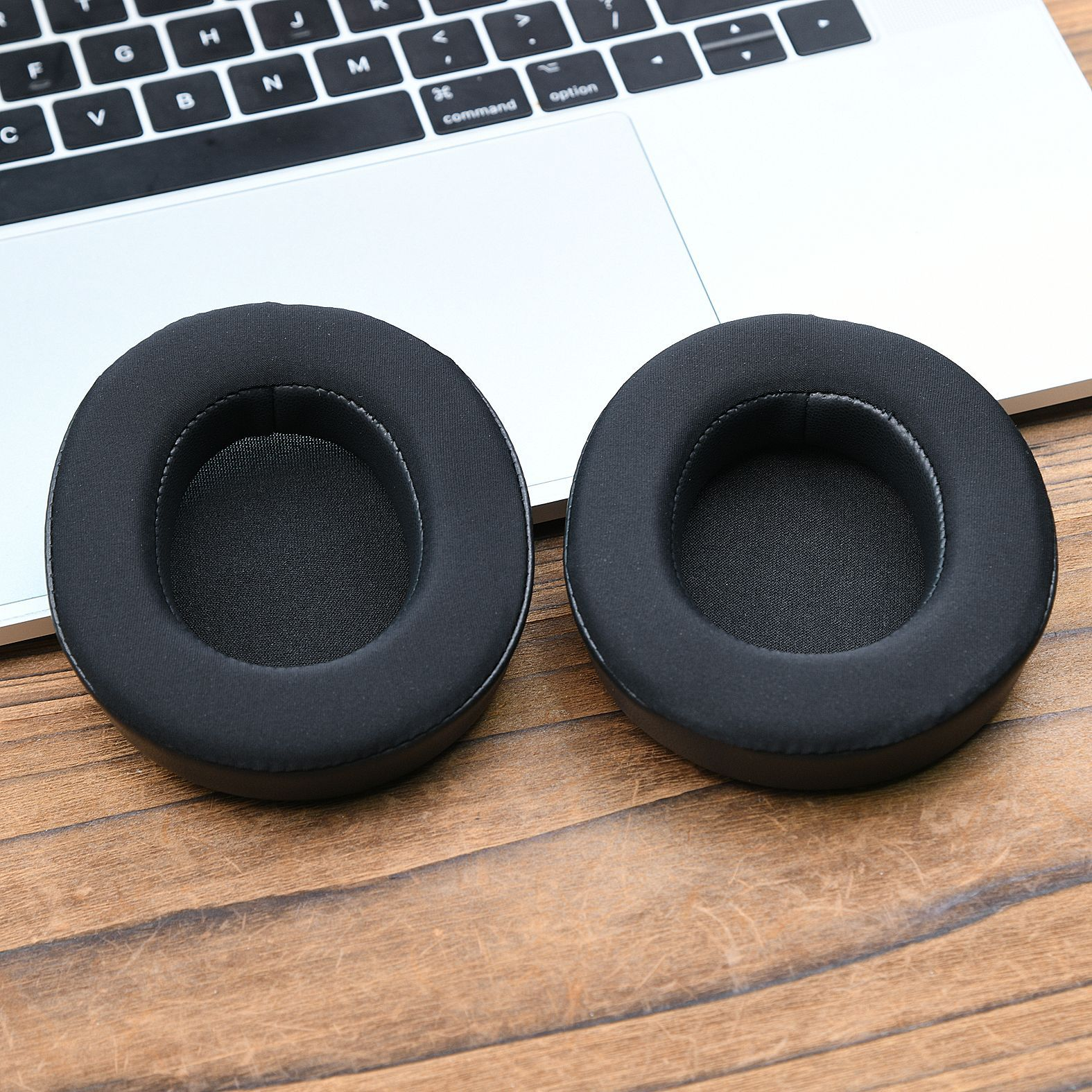 Due cuscinetti auricolari neri per cuffie appoggiati sulla tastiera di un laptop. I cuscinetti sono circolari.