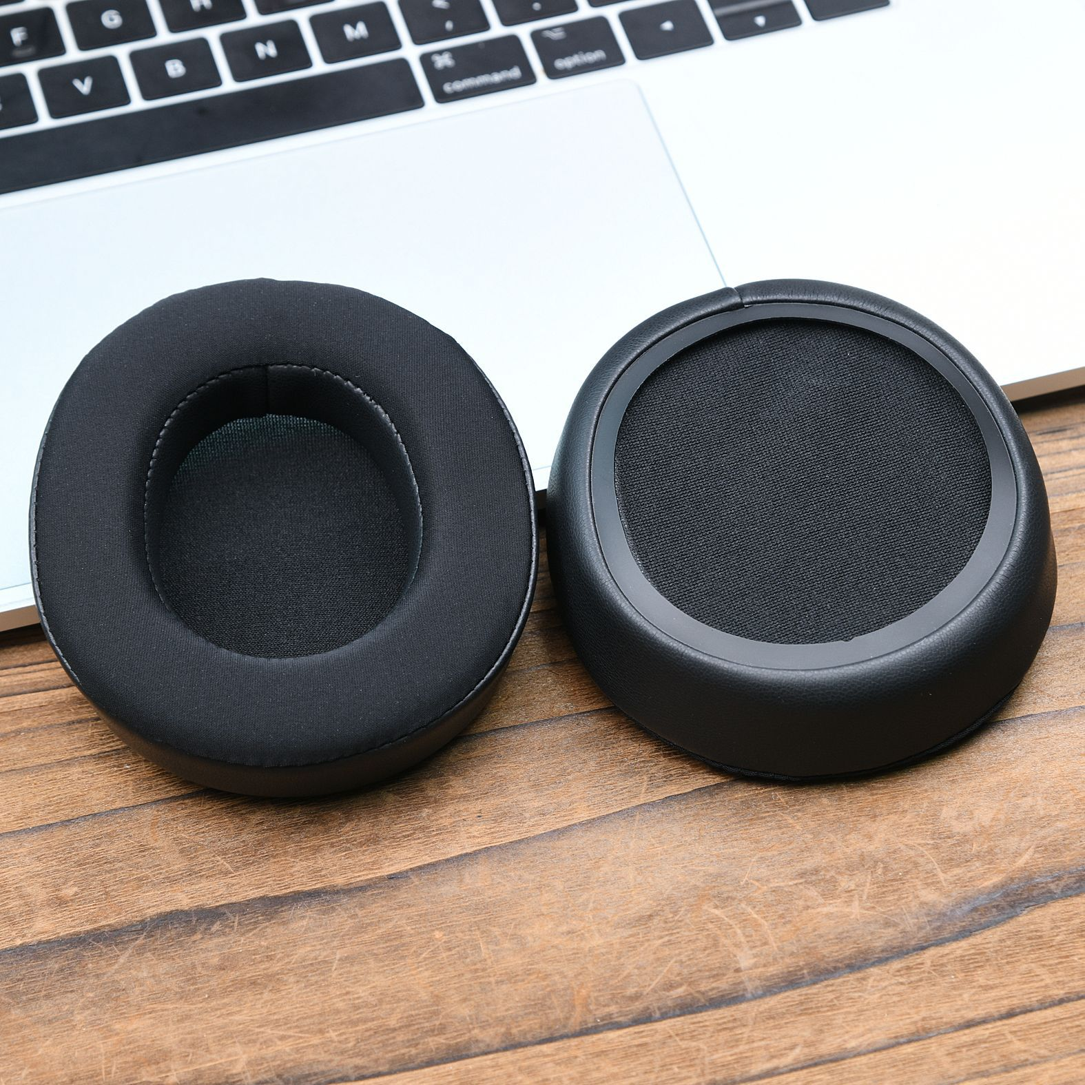 Due cuscinetti auricolari neri per cuffie appoggiati sulla tastiera di un laptop. I cuscinetti sono circolari. Uno ha l'interno in rete.