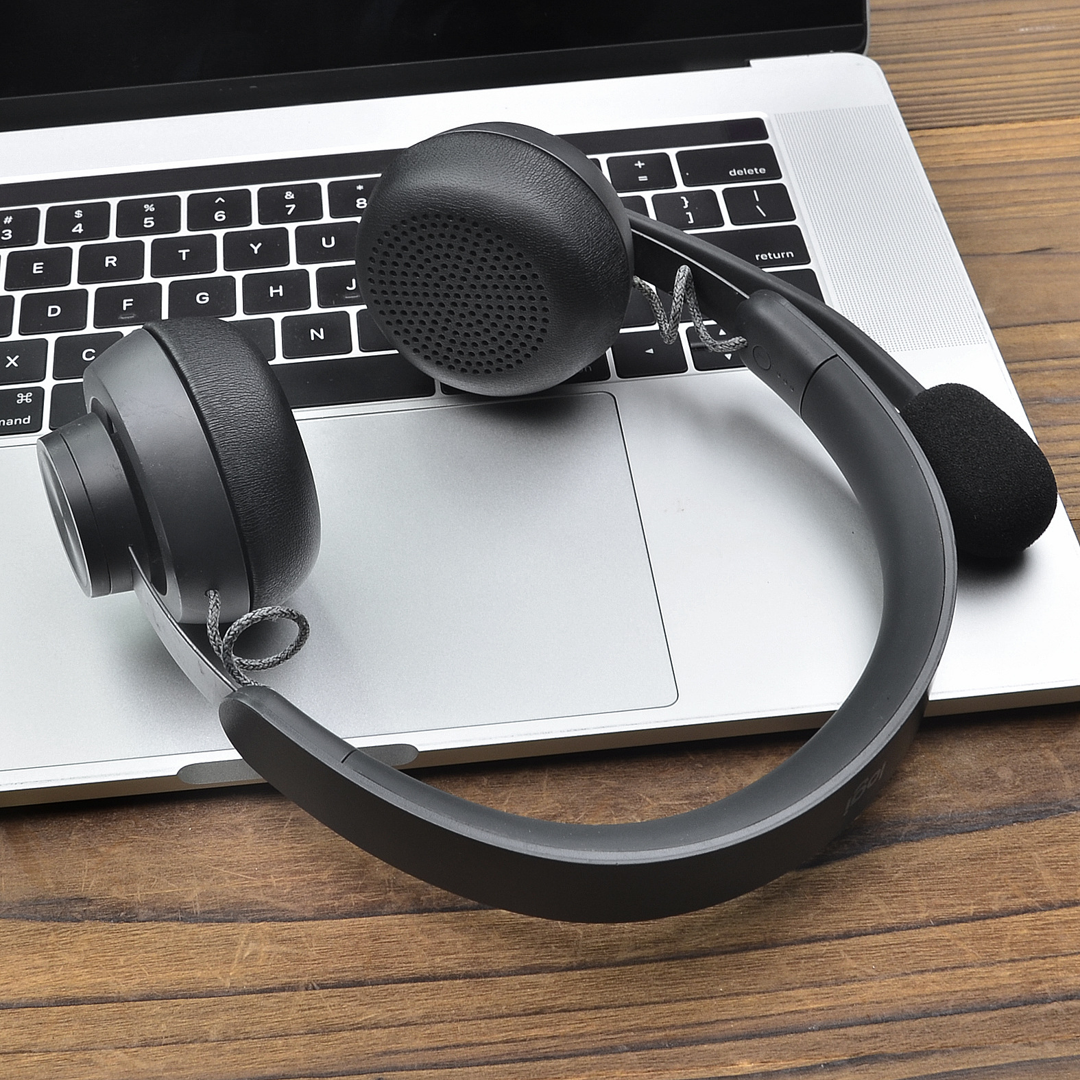 Schwarzes Headset mit Mikrofon auf einem Laptop. Der Laptop liegt auf Holz.