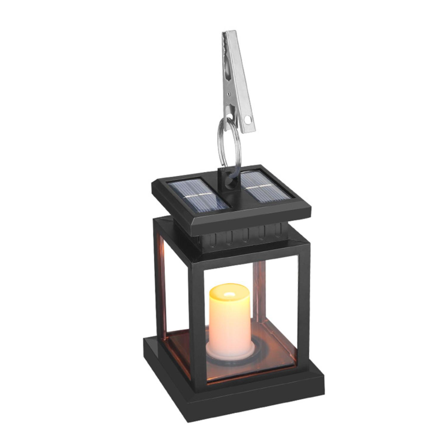 Eine schwarze Solar-Laterne mit kerzenähnlichem Licht, die an einem Metallclip vor weißem Hintergrund hängt.