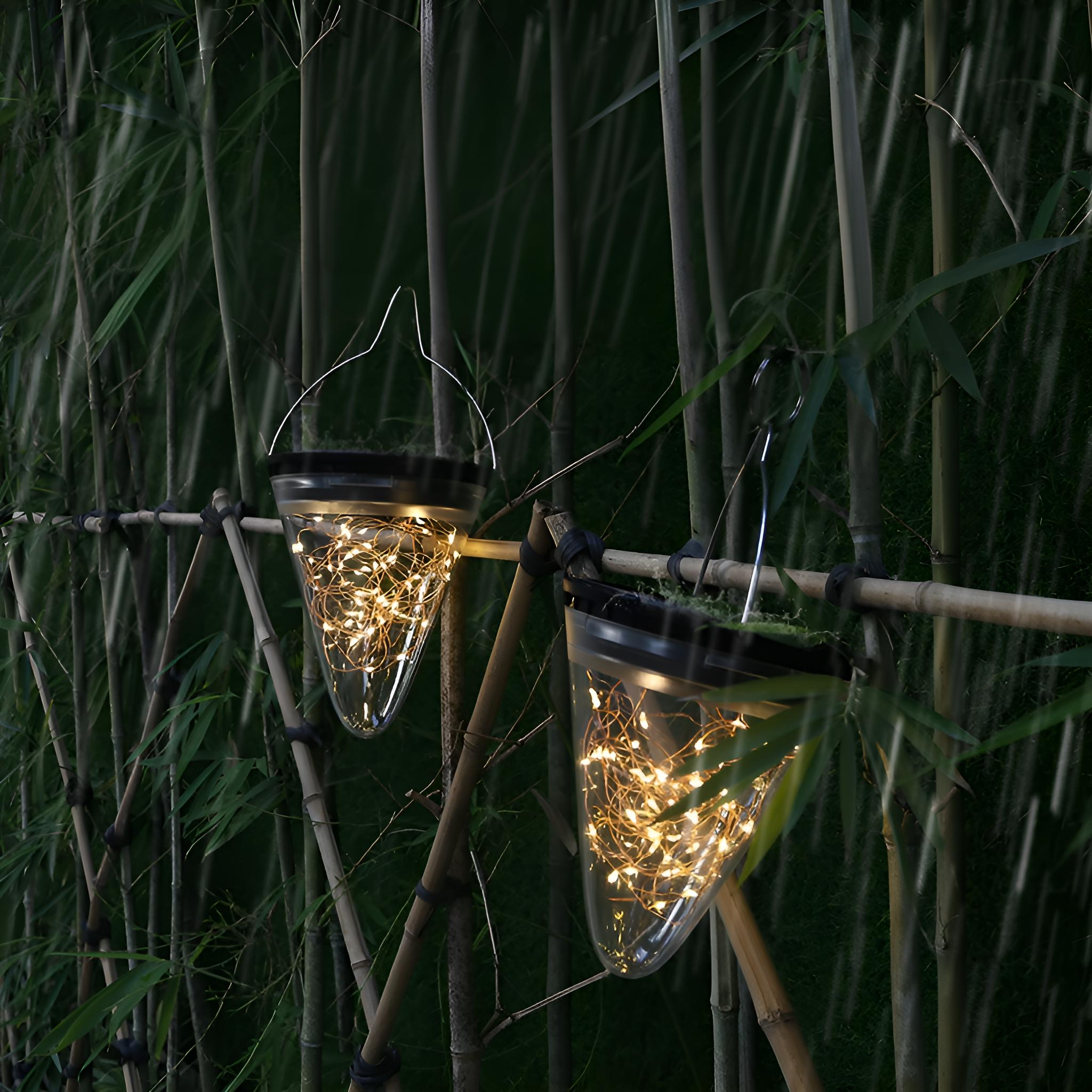 Zwei kegelförmige Solarlichter mit Lichterketten, die nachts an einem Bambuszaun hängen.