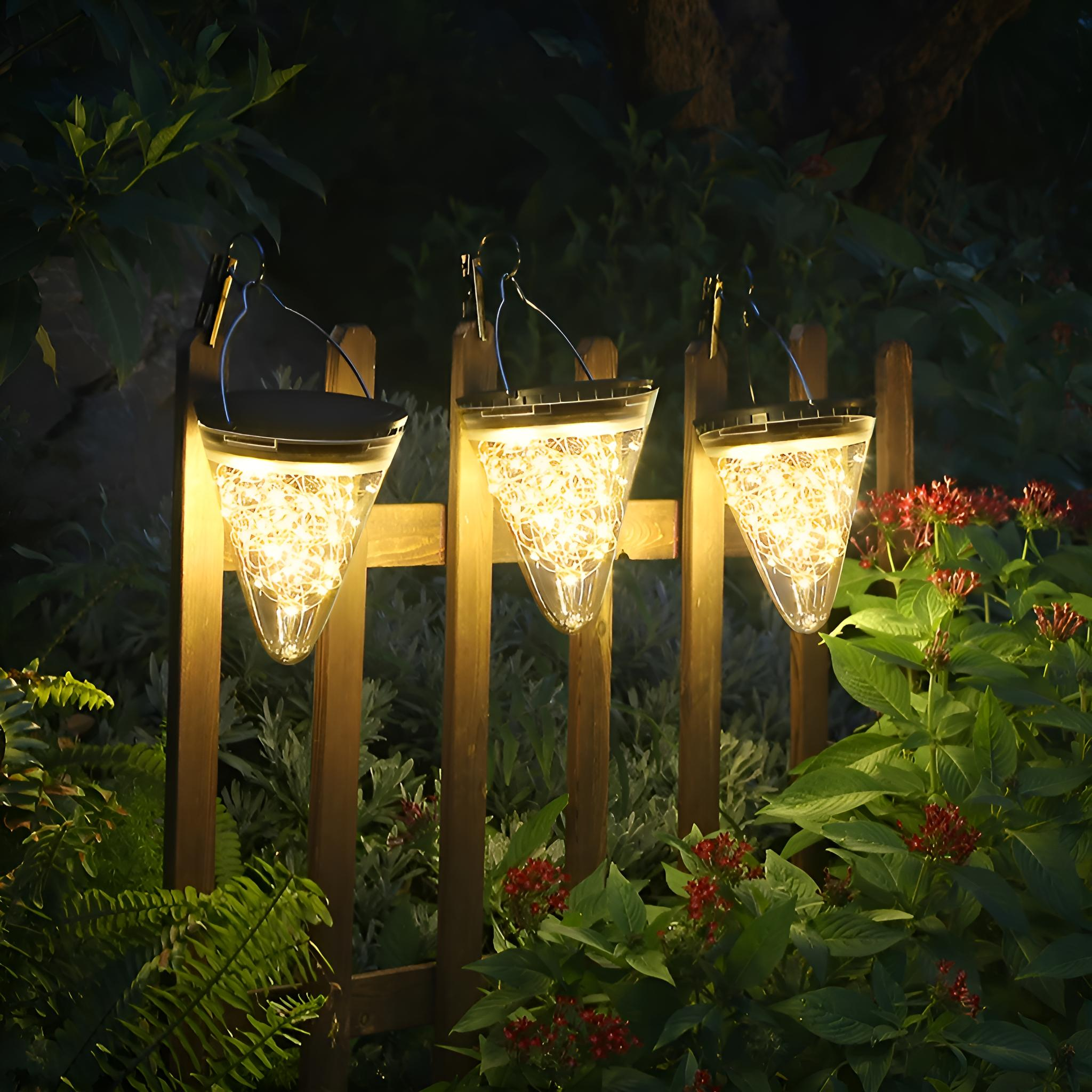 Drei kegelförmige Solarlichter mit Lichterketten, die nachts an einem Holzzaun hängen.