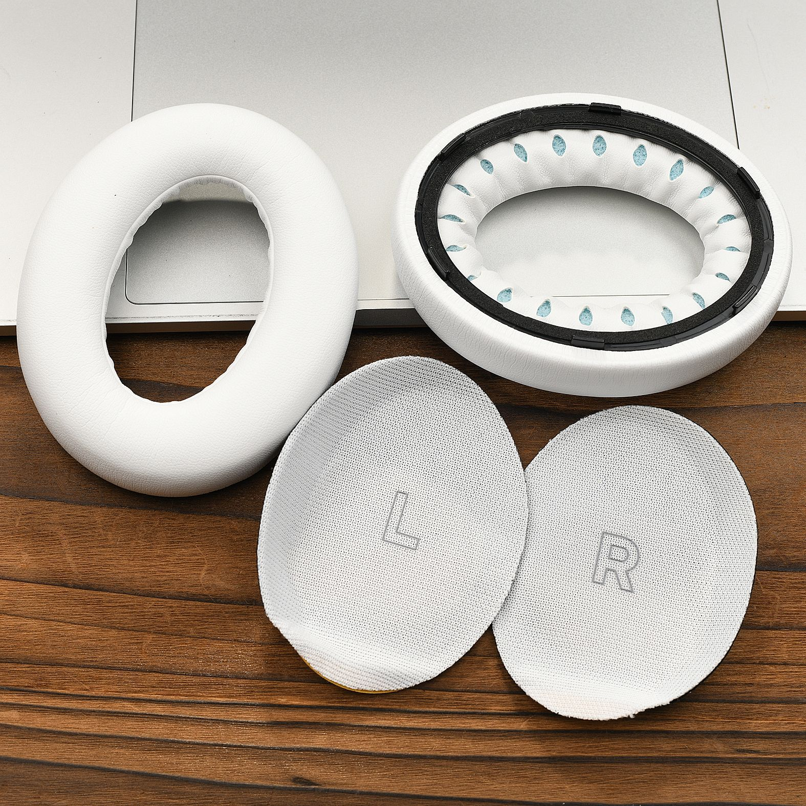 Un cuscinetto auricolare bianco per cuffie, due cuscinetti interni con lettere L e R su legno e laptop.