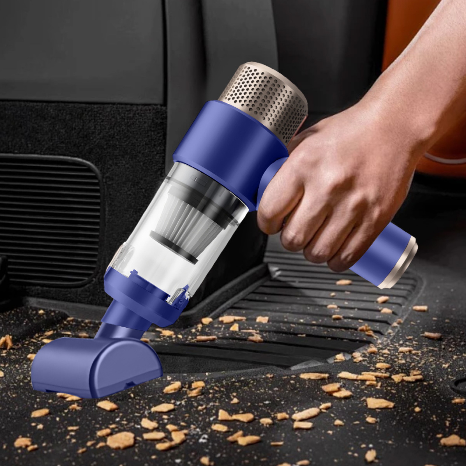 Eine Hand benutzt einen blau-silbernen Handstaubsauger auf einem Autoboden mit Schmutz.