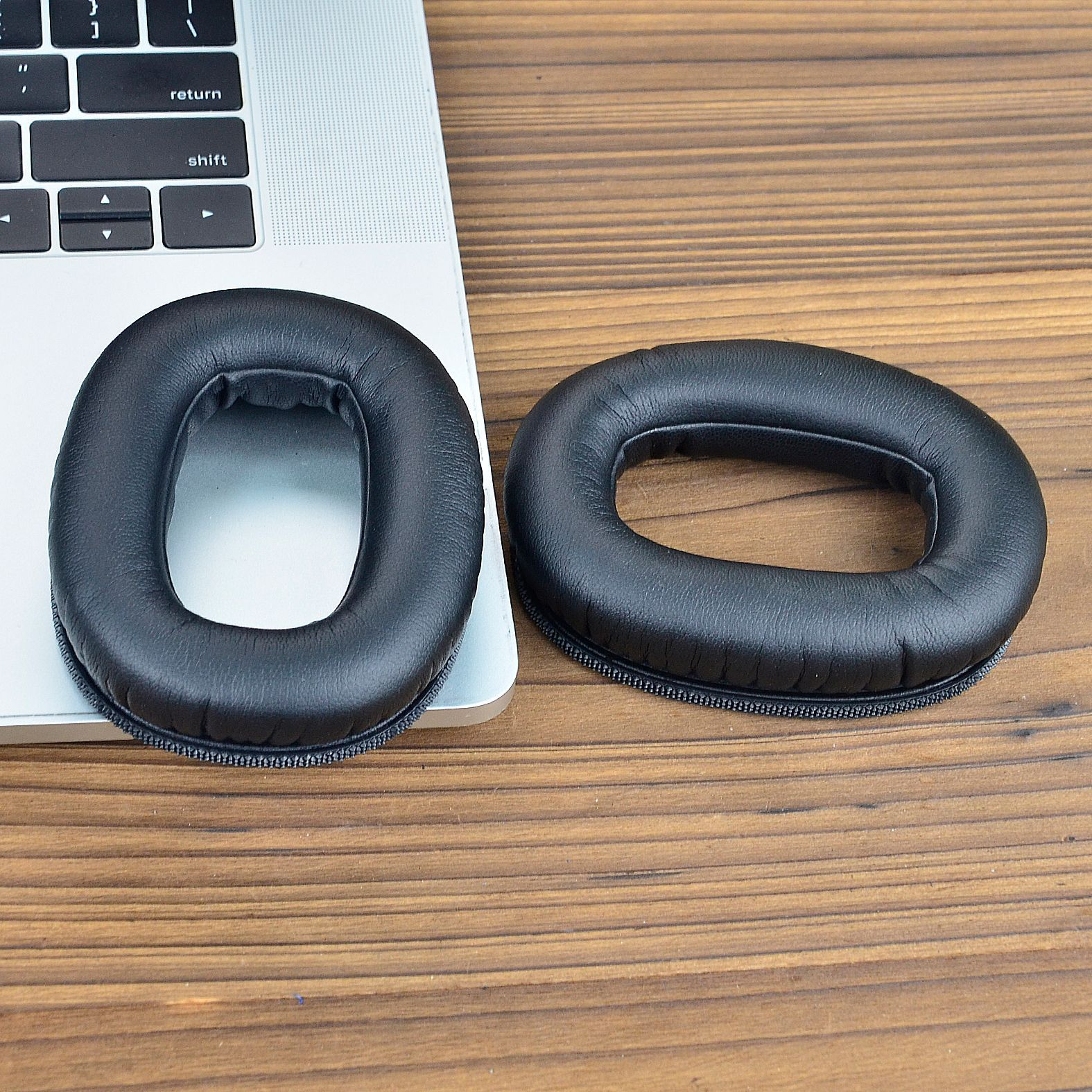 Due cuscinetti auricolari neri posizionati sulla tastiera di un laptop su una superficie di legno.