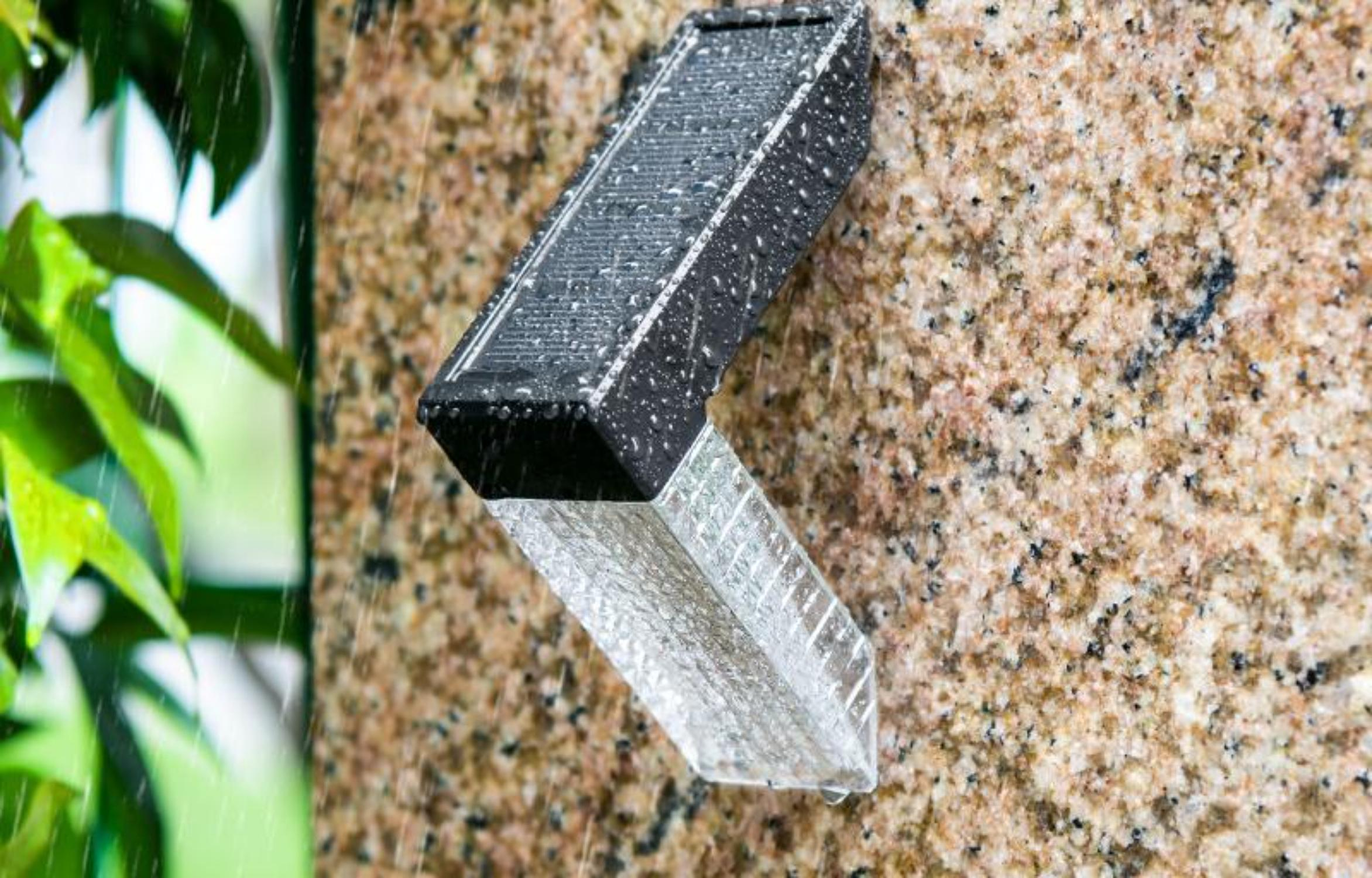 Solar-Stufenlicht mit Regeneffekt an einer Granitwand, Licht scheint nach unten, schwarzer Rahmen, klarer Kunststoff.