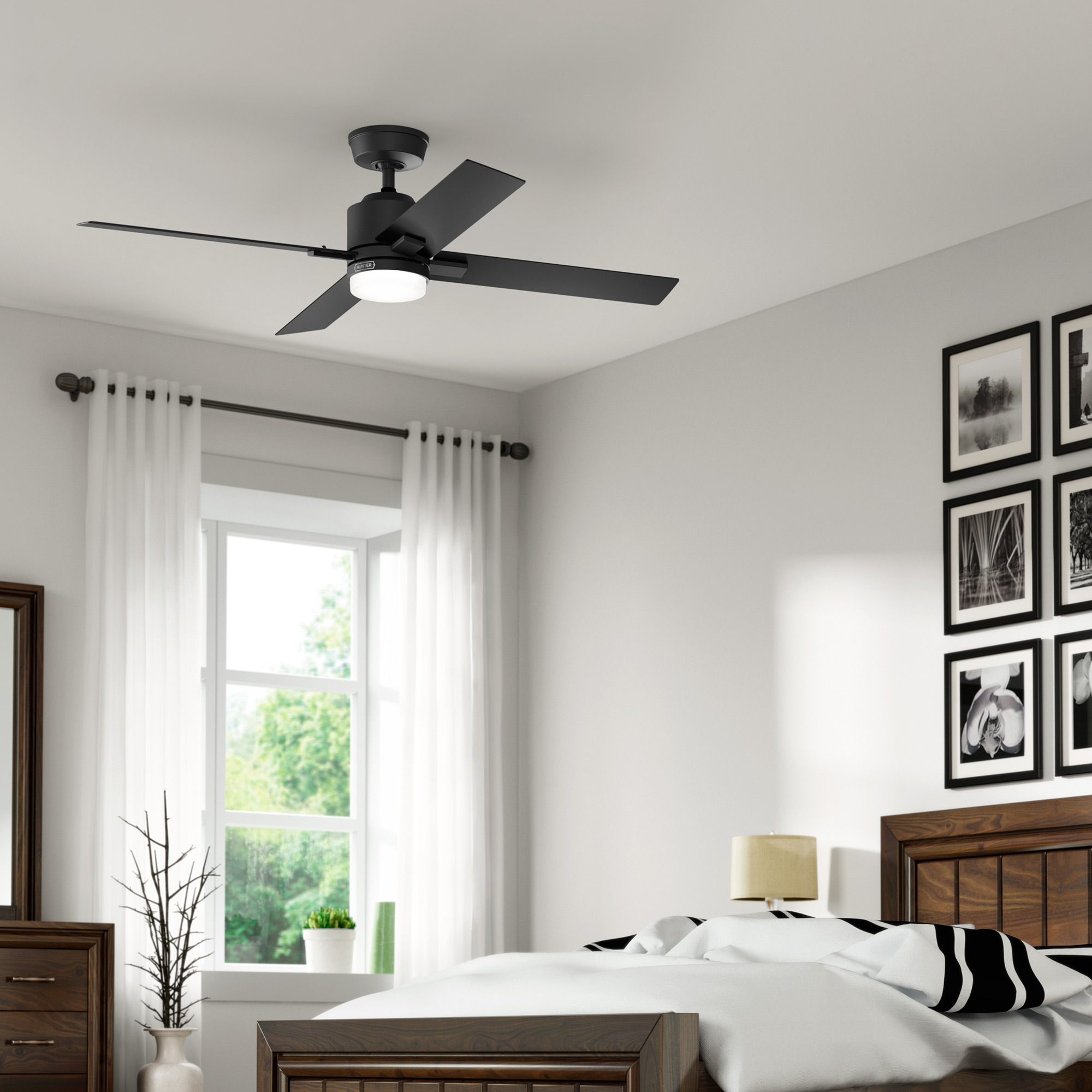 Schlafzimmer mit schwarzem Deckenventilator, weißen Vorhängen und hölzernem Bettrahmen. Bilder an der Wand.