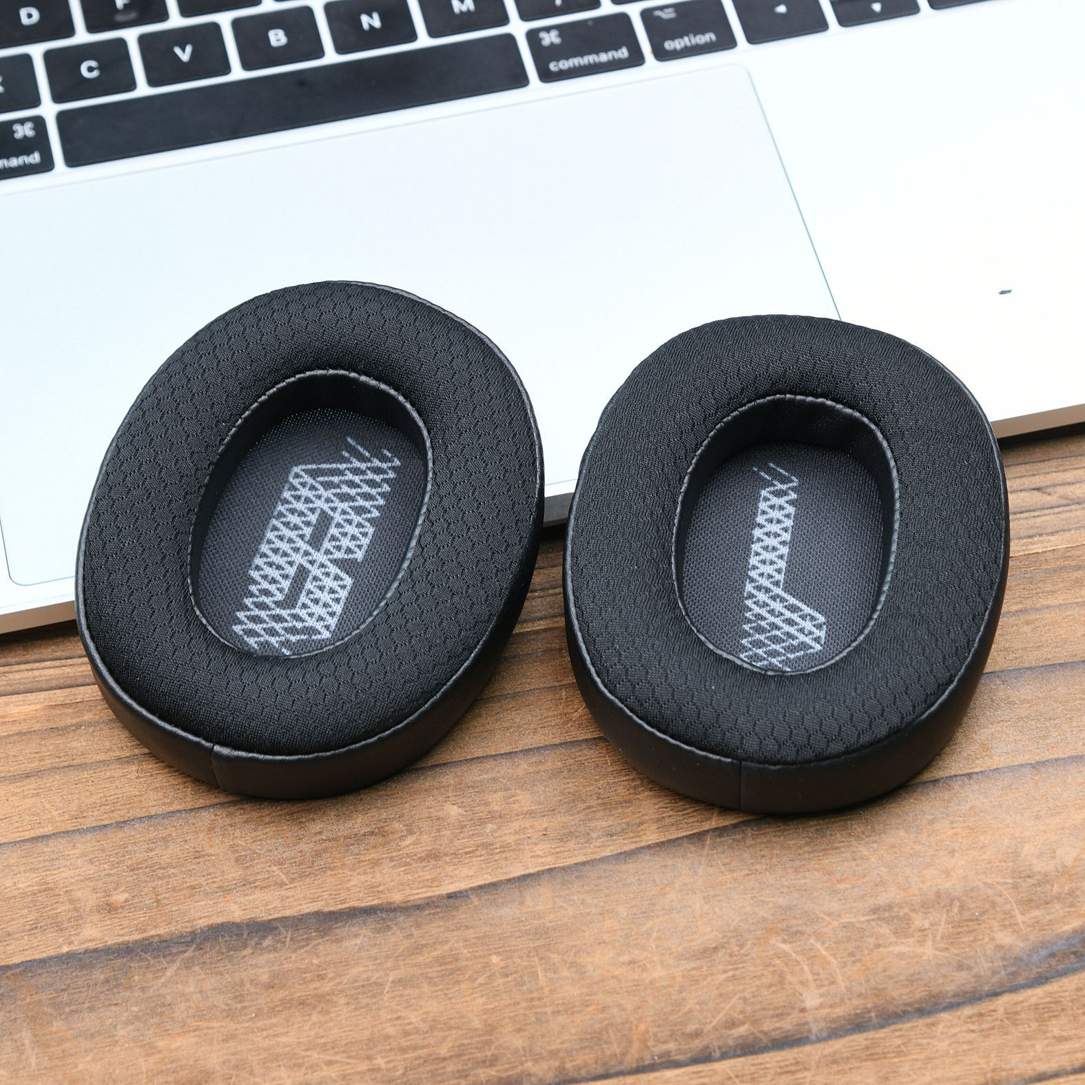 Due cuscinetti neri per cuffie su una superficie in legno, con il logo JBL visibile.