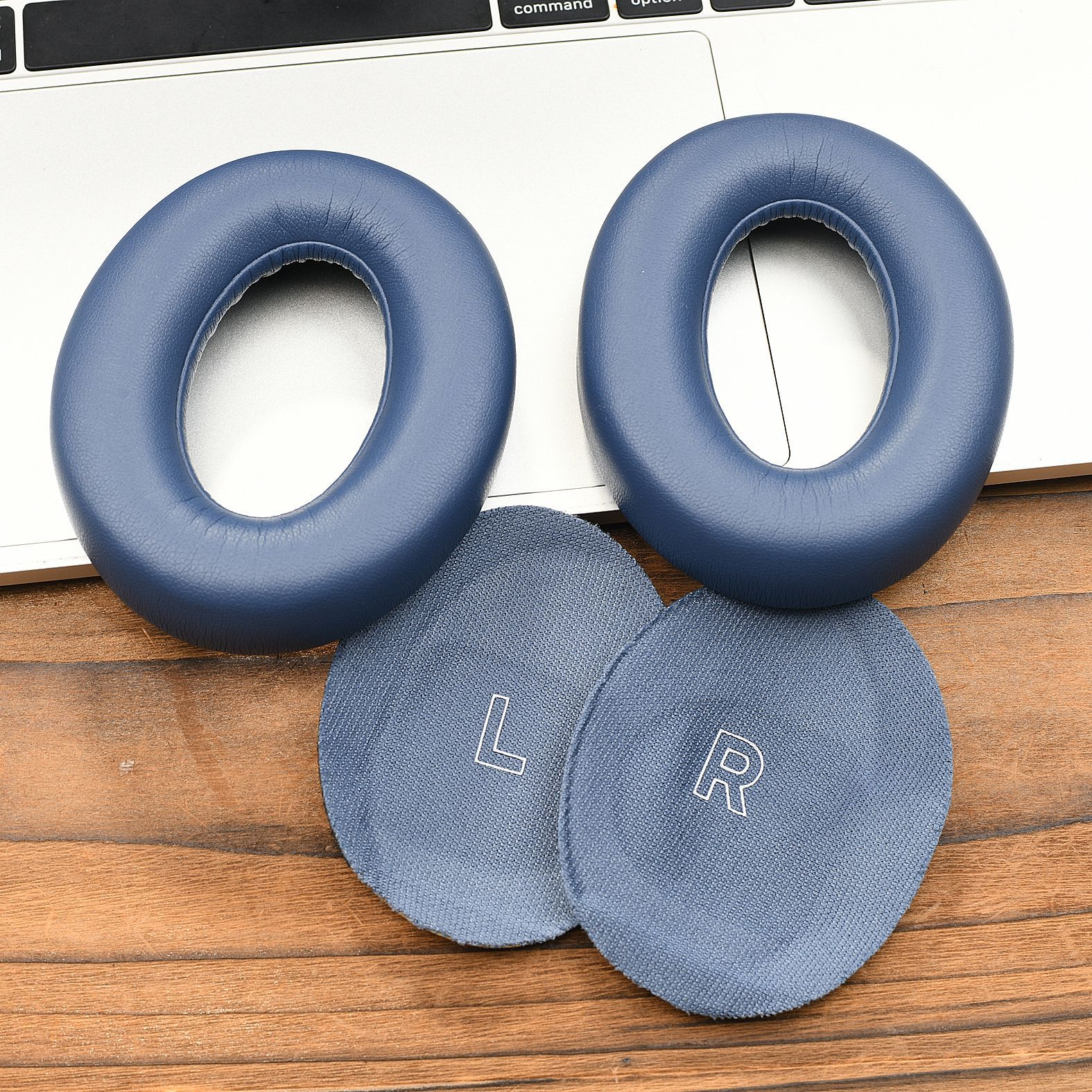 Zwei blaue Ohrmuscheln und zwei kleine graue Pads, markiert mit 'L' und 'R', liegen auf einer Holzoberfläche.