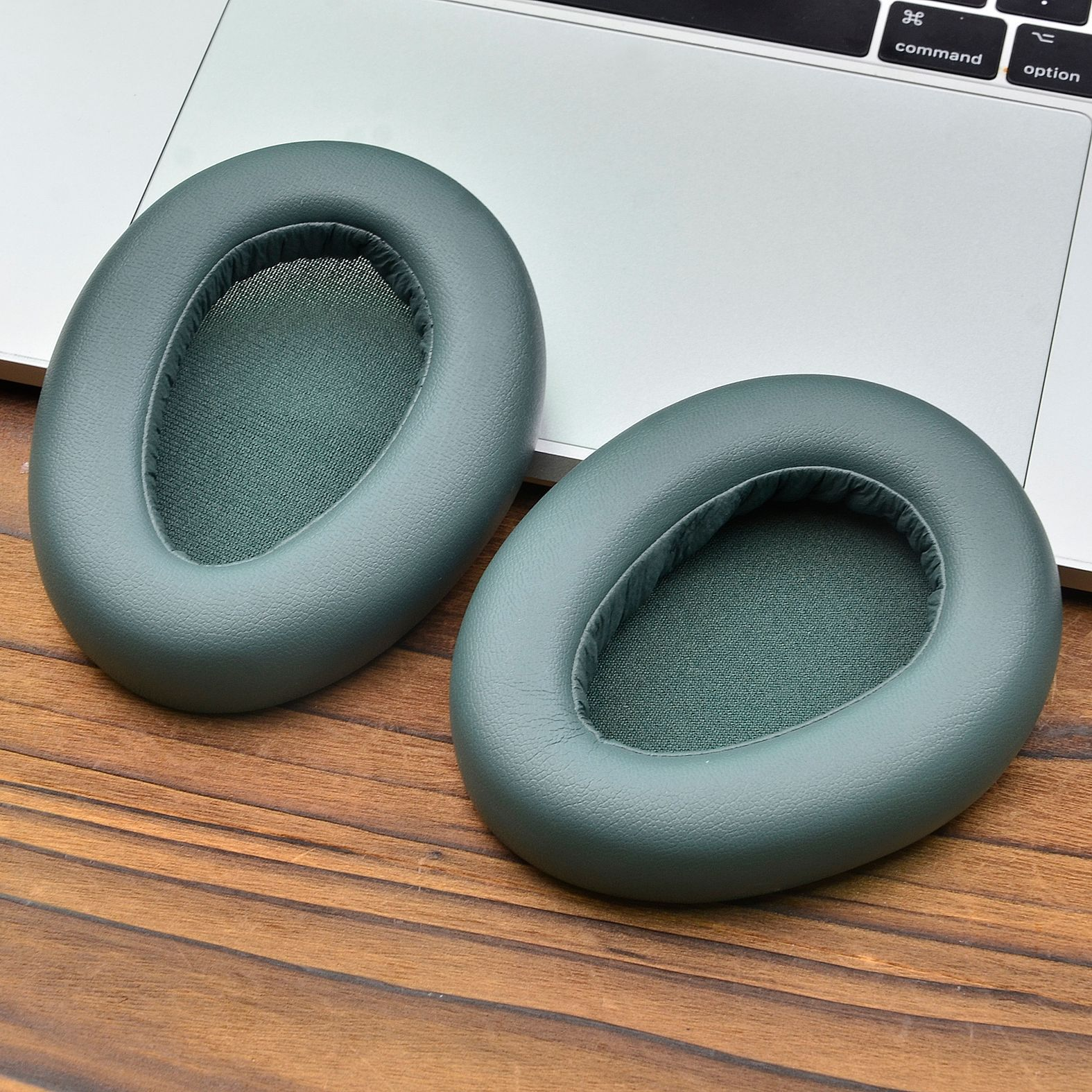 Due cuscinetti auricolari verde acqua su una superficie di legno, con un laptop sullo sfondo.