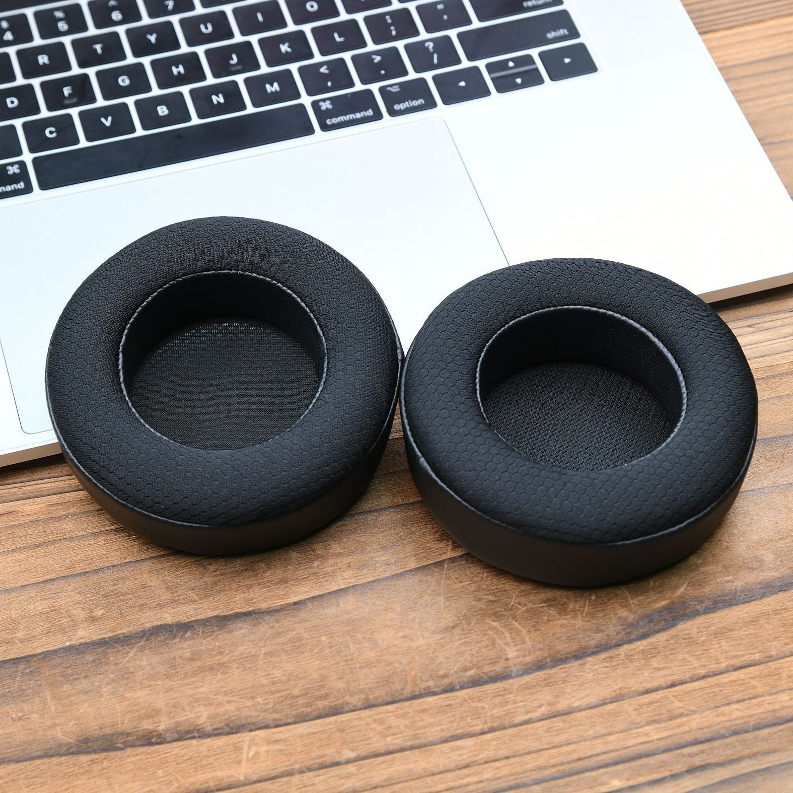 Due cuscinetti auricolari neri per cuffie su un laptop. I cuscinetti sono circolari con un centro in rete.