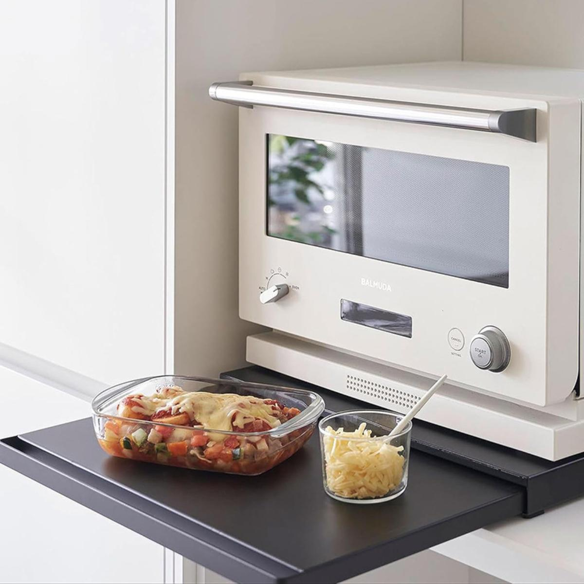 Eine Mikrowelle auf einer Theke mit Essen. Es gibt eine Glasschale mit Essen und eine kleine Schüssel mit Käse.