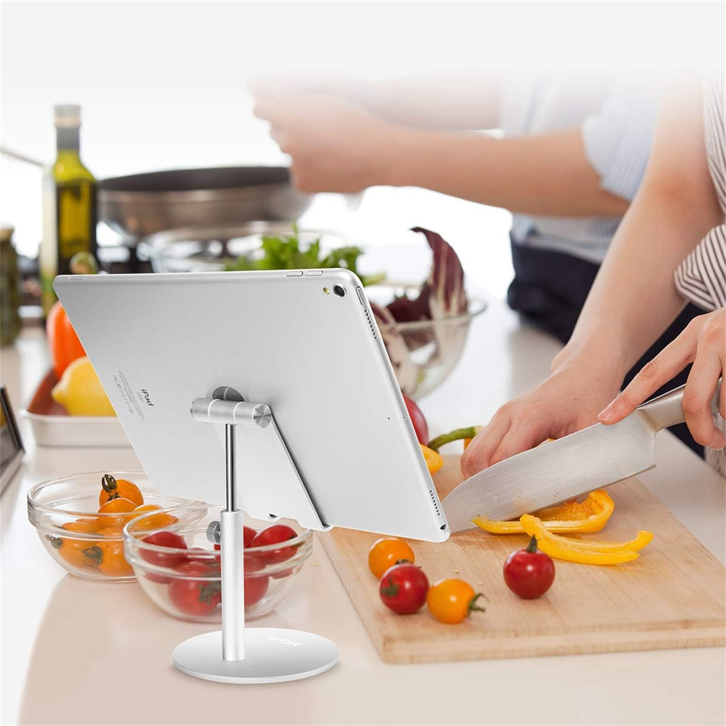 Person schneidet Gemüse, Tablet auf Ständer. Tablet wird beim Kochen verwendet.