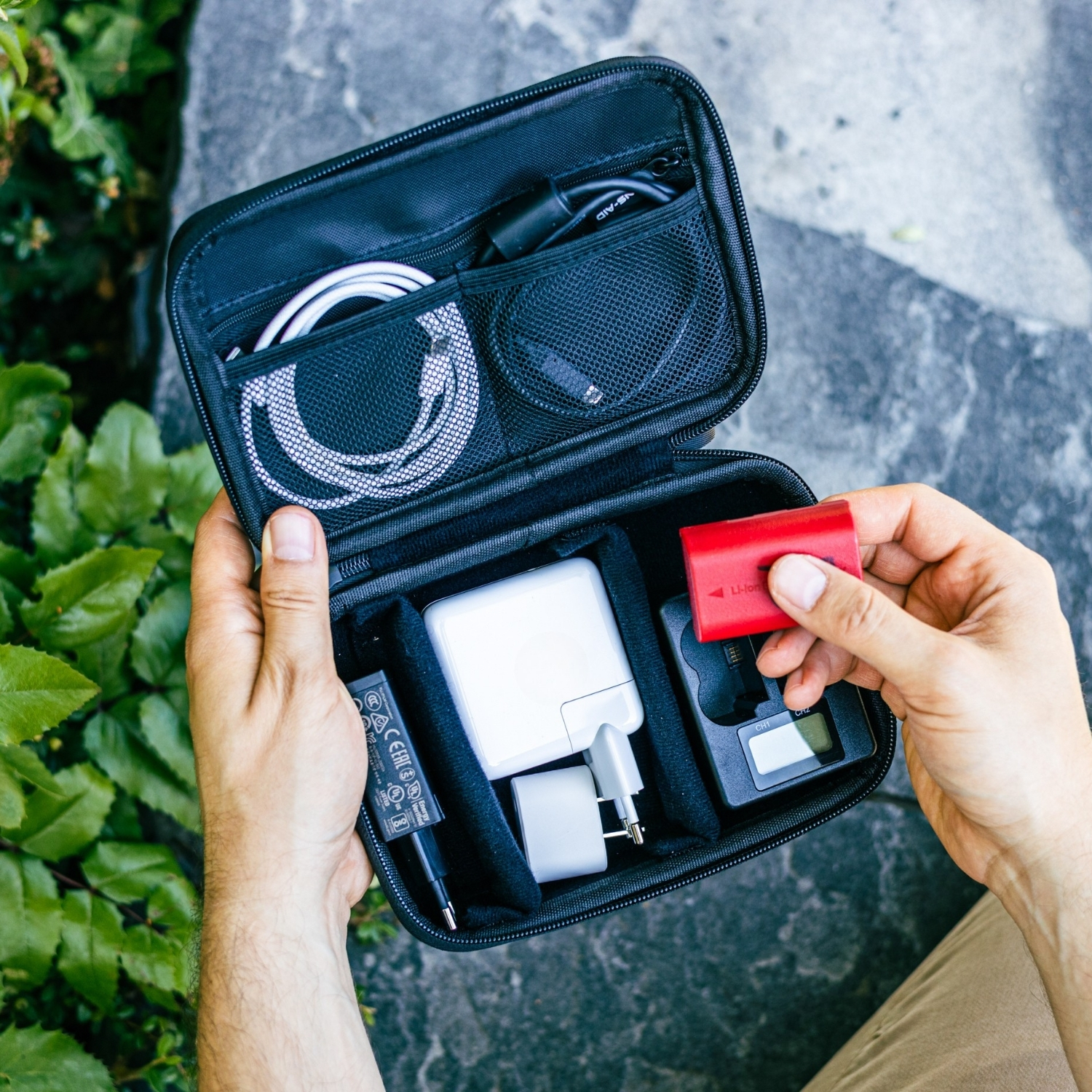 Hände halten eine schwarze Tasche mit Ladeausrüstung. Eine rote Batterie wird hinzugefügt.