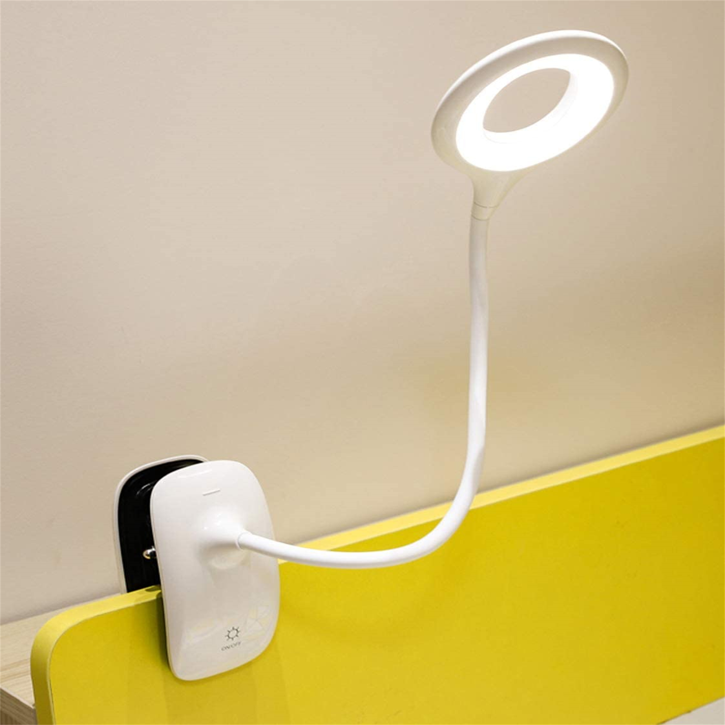 Weiße Schreibtischlampe an gelber Oberfläche befestigt. Die Lampe hat ein kreisförmiges Licht und einen flexiblen Arm.
