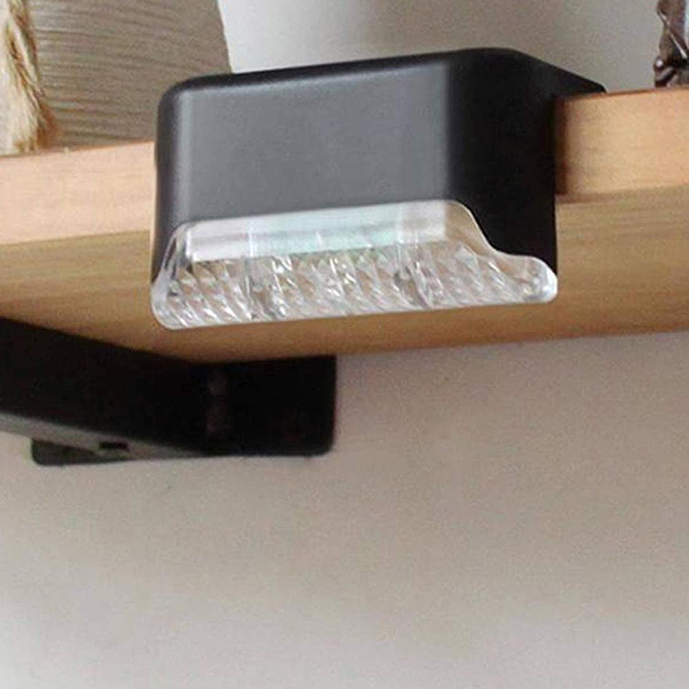 Eine schwarze Lampe mit einem klaren, strukturierten Boden. Die Lampe ist an einem Holzregal befestigt.
