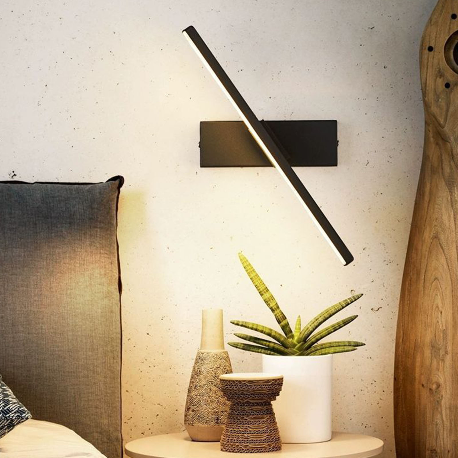 Eine schwarze Wandleuchte mit einer abgewinkelten weißen Lichtleiste, platziert an einer hellen Wand.