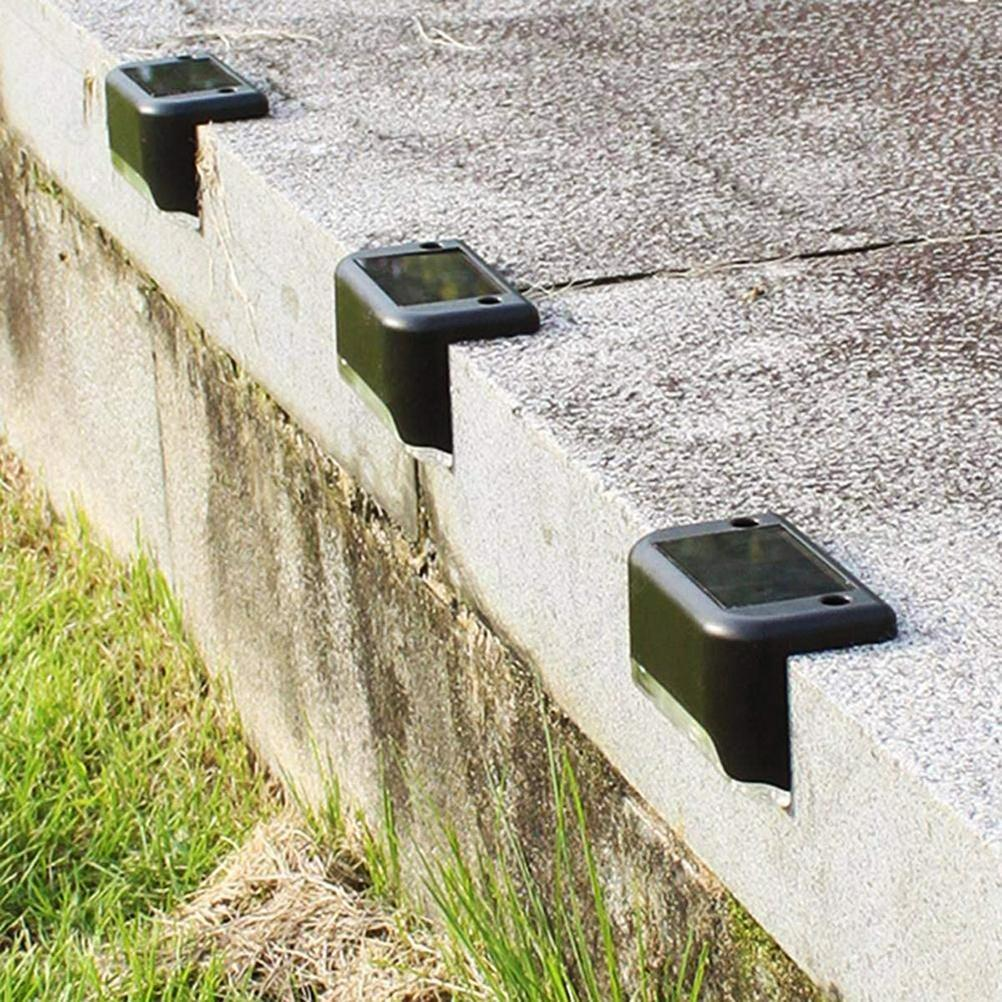 Drei schwarze Solarleuchten auf einer Betonstufe. Gras am unteren Ende der Stufe.