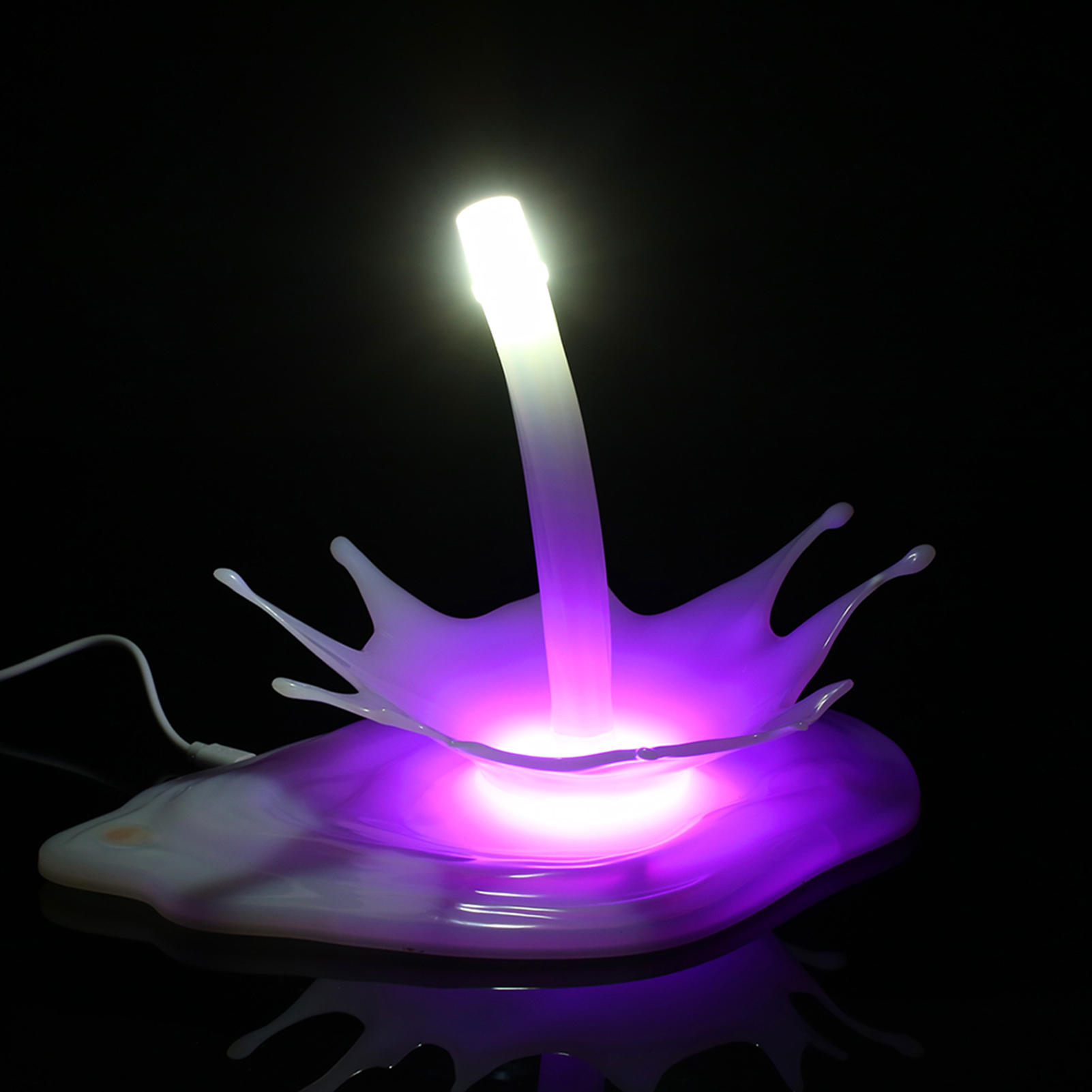 Eine lila-weiße Lampe mit Spritzdesign. Die Lampe steht auf einer schwarzen Oberfläche. Der Hintergrund ist schwarz.