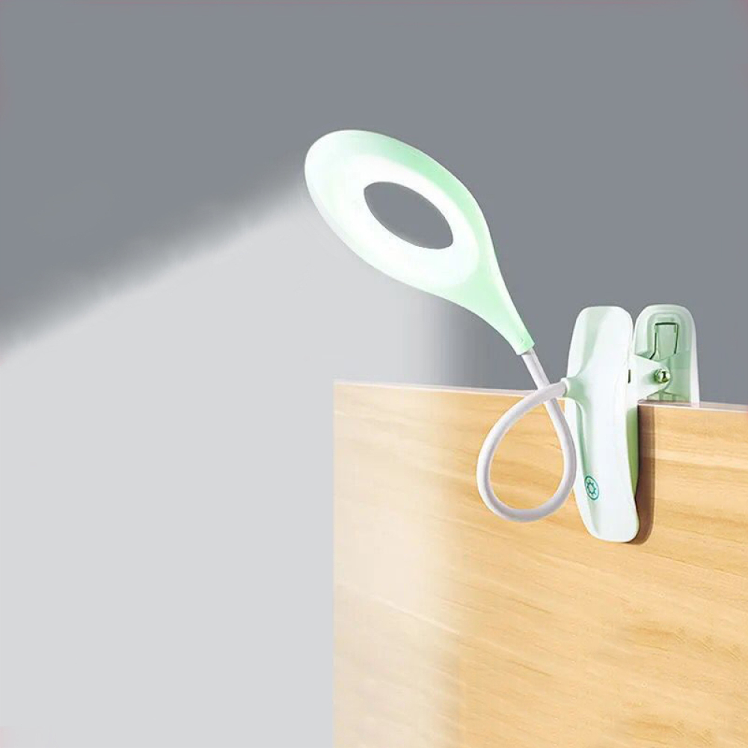 Eine grüne Schreibtischlampe mit flexiblem Hals und Clip. Das Licht ist an und scheint.