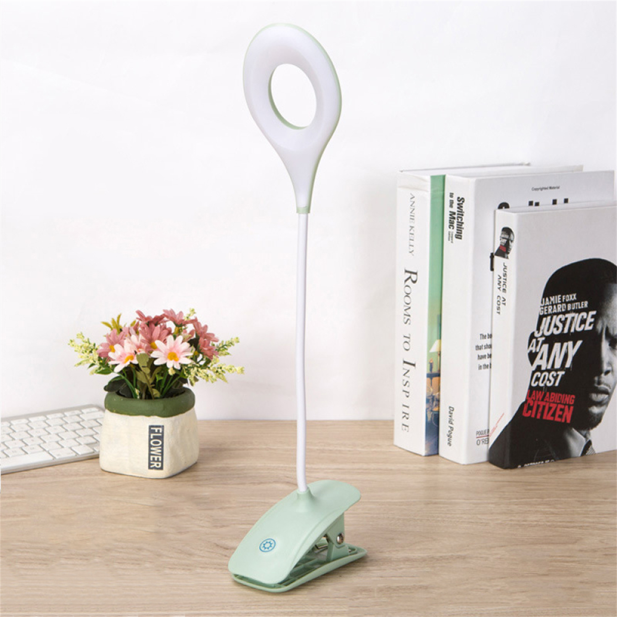 Eine mintfarbene Schwanenhalslampe steht auf einem Holzschreibtisch mit Büchern und Blumen im Hintergrund.