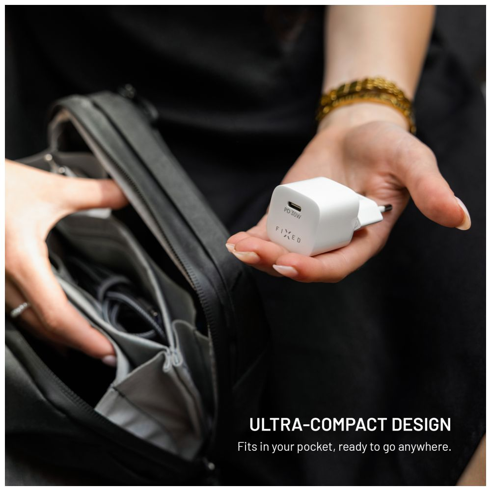 Eine Hand hält ein weißes Ladegerät mit dem FIXED-Logo und eine schwarze Tasche im Hintergrund.