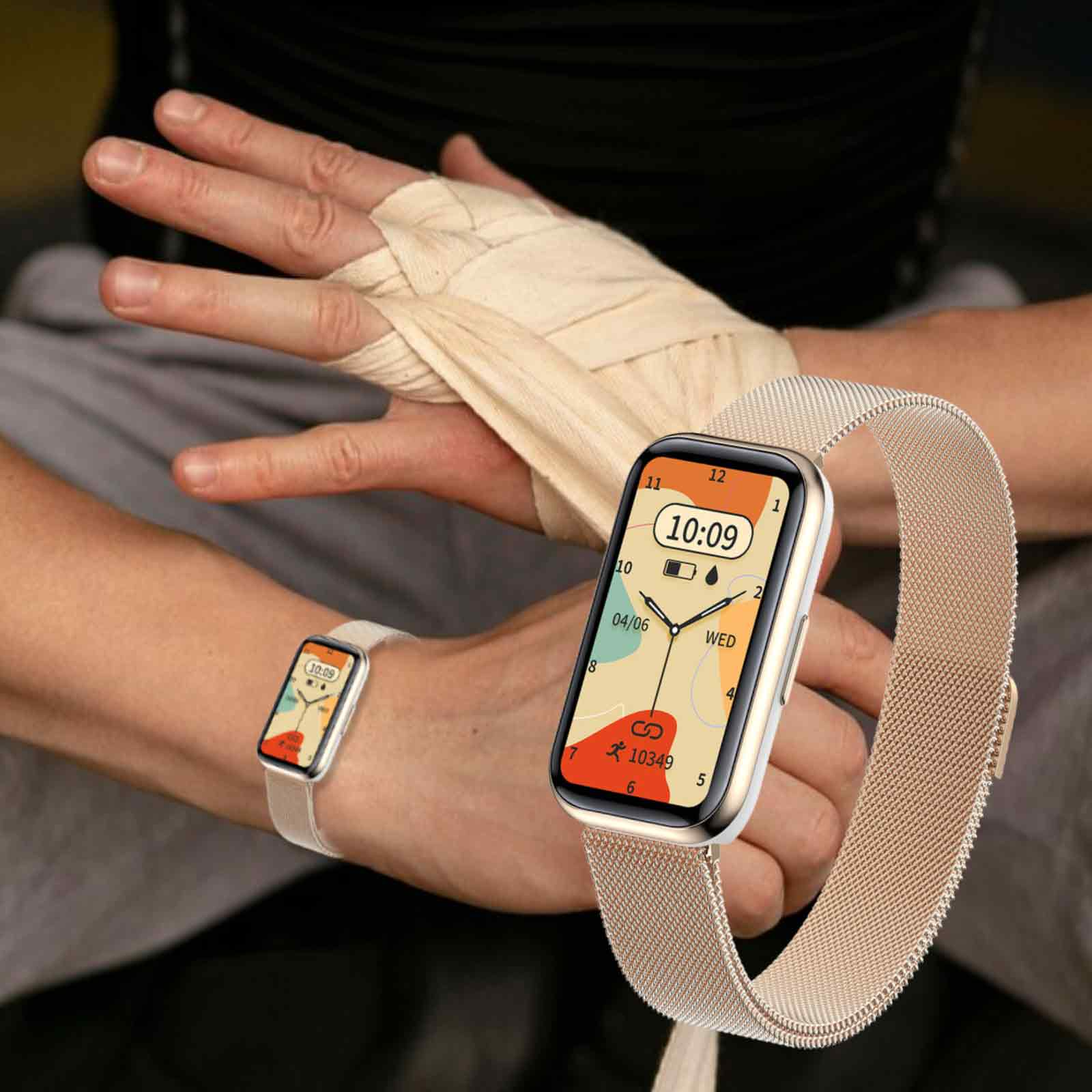 Eine Smartwatch am Handgelenk mit goldenem Armband, die Zeit und Datum anzeigt. Eine andere Uhr im Hintergrund.