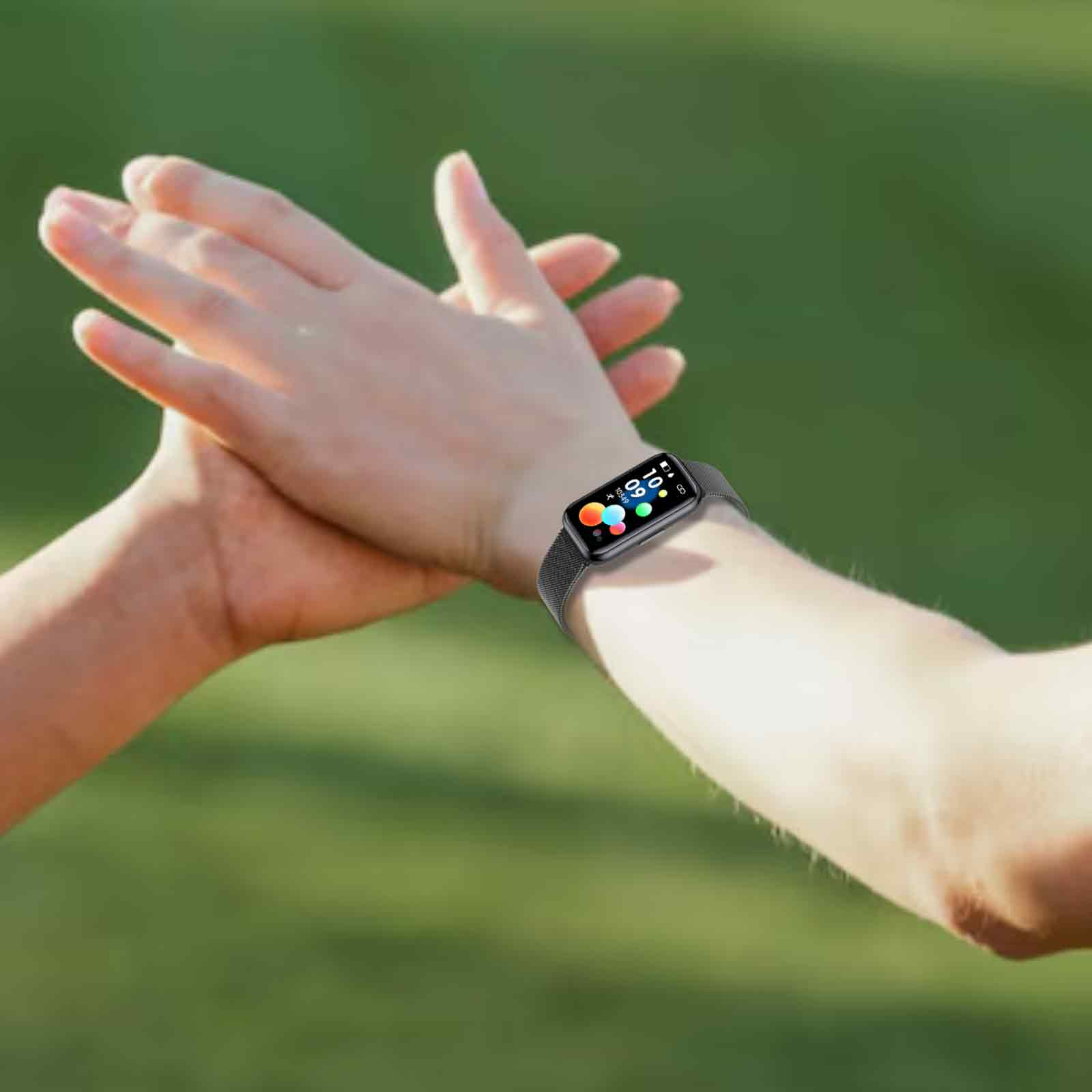 Hände einer Person mit Smartwatch am Handgelenk. Der Hintergrund ist ein verschwommenes grünes Feld.