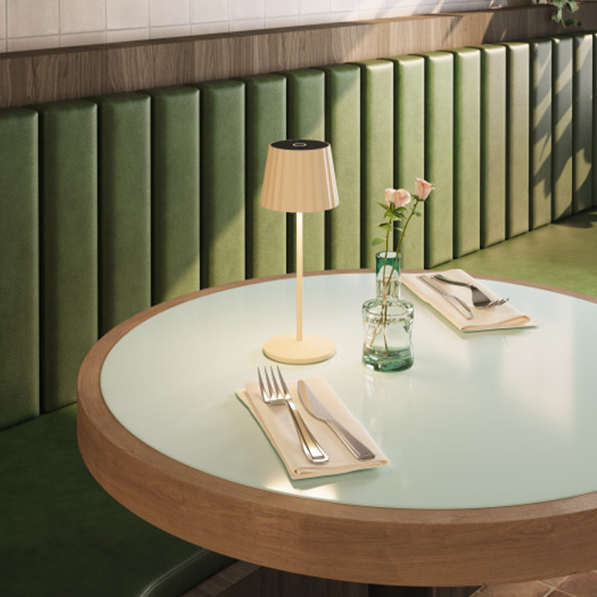 Ein gedeckter Tisch mit Lampe, Blumen und Besteck. Grüne Sitzbank im Hintergrund.