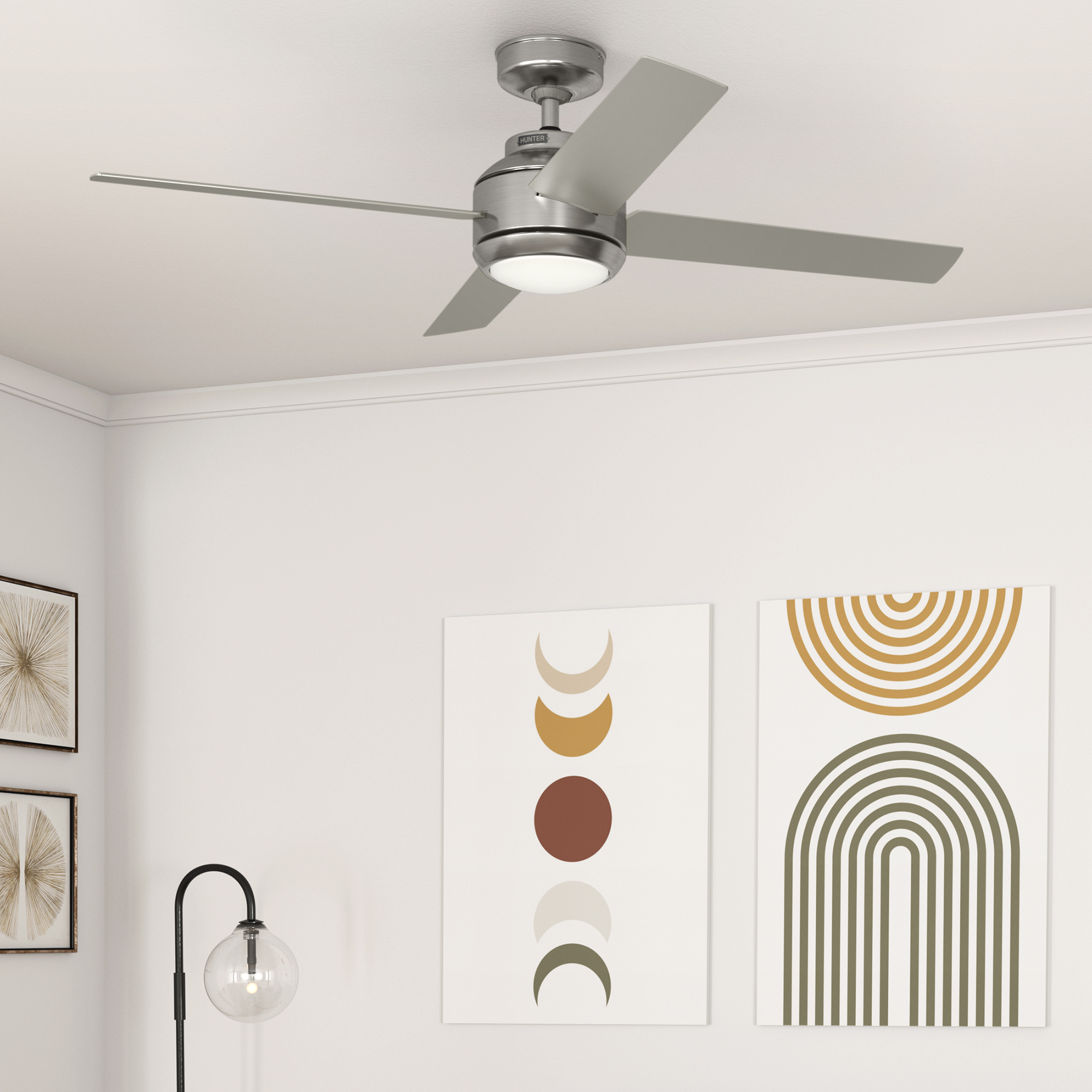 Ein Deckenventilator mit vier Flügeln, hellgrauen Flügeln und einer Oberfläche aus gebürstetem Nickel. Der Raum hat Kunst an der Wand.