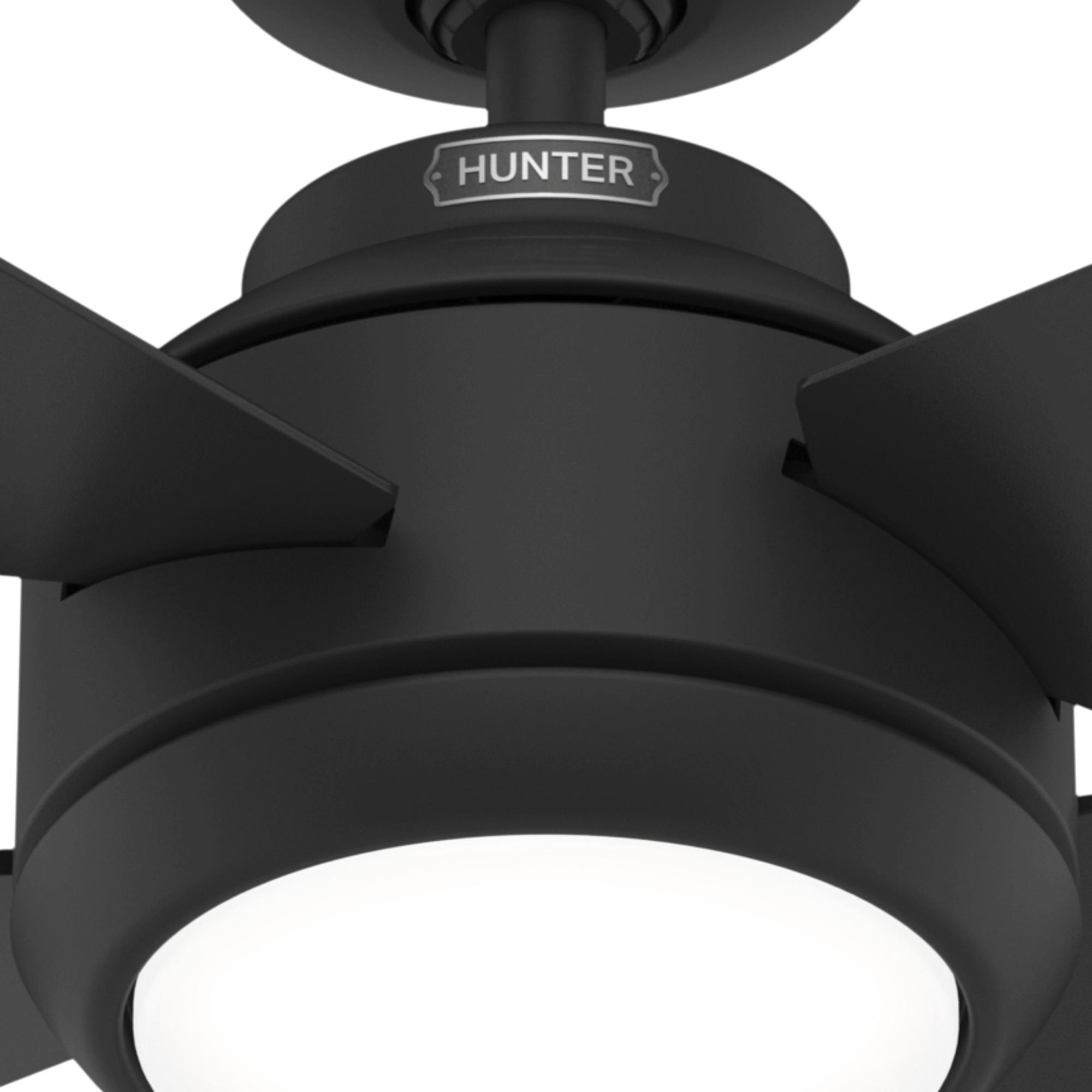 Nahaufnahme eines schwarzen Deckenventilators mit dem Markennamen 'HUNTER' auf dem Motorgehäuse und weißem Licht.