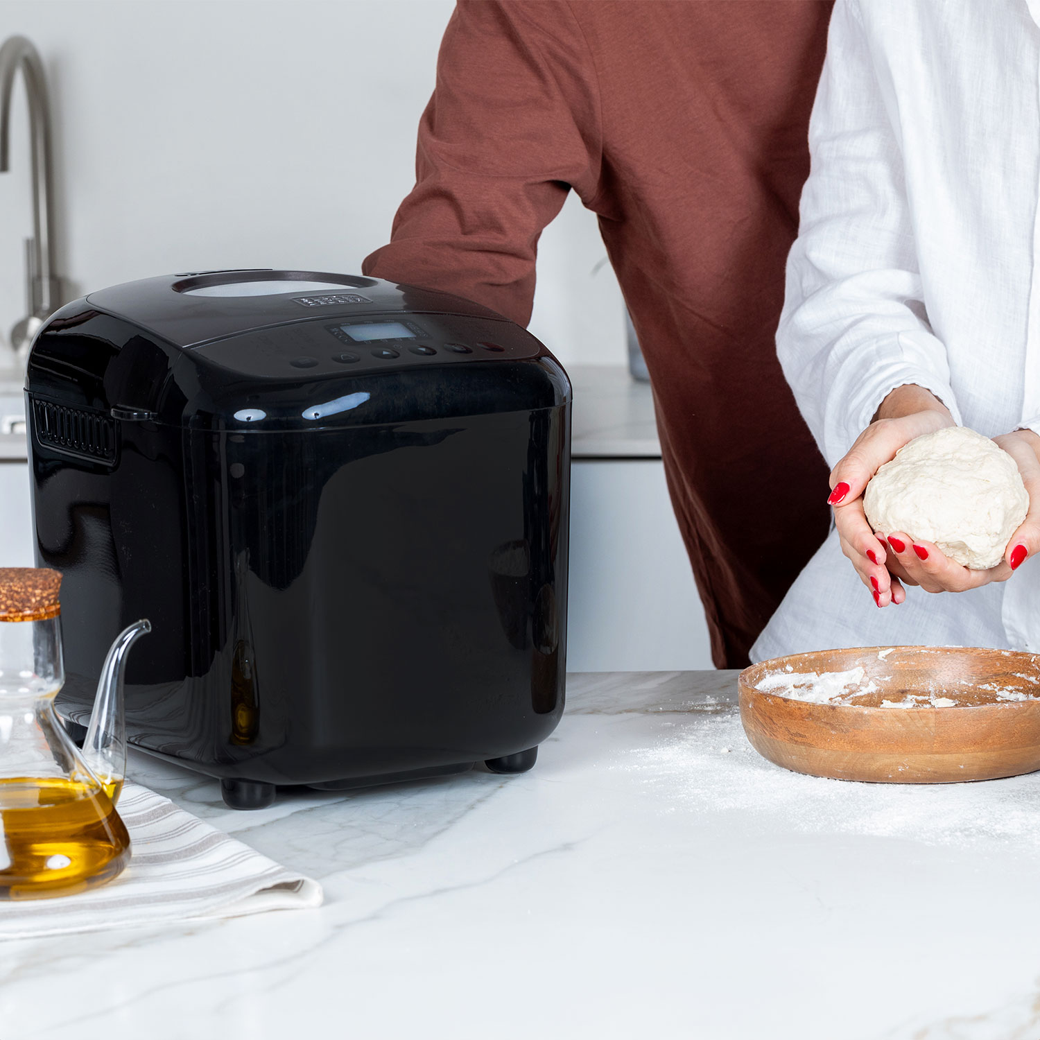 Een zwarte broodbakmachine op een marmeren aanrecht met een persoon die deeg vasthoudt.