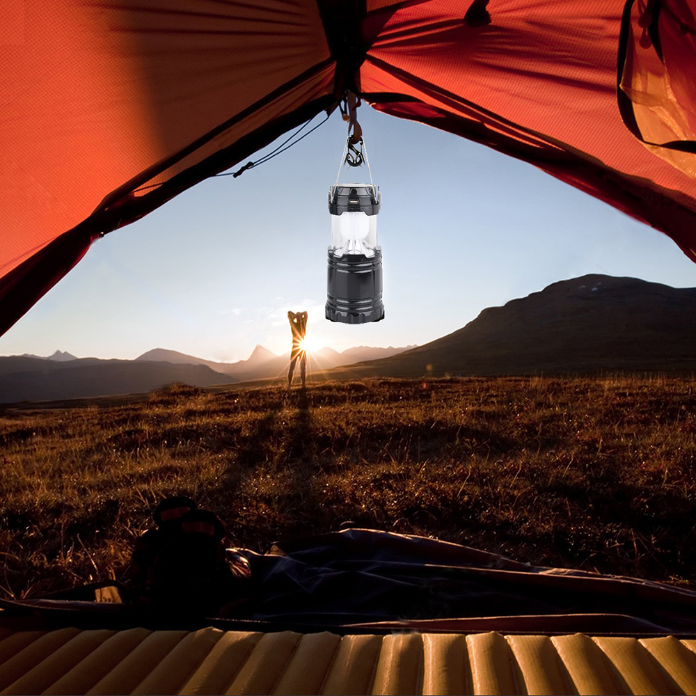 Eine Campinglaterne hängt in einem Zelt, mit Blick auf den Sonnenuntergang durch die Öffnung. Die Landschaft umfasst Berge.