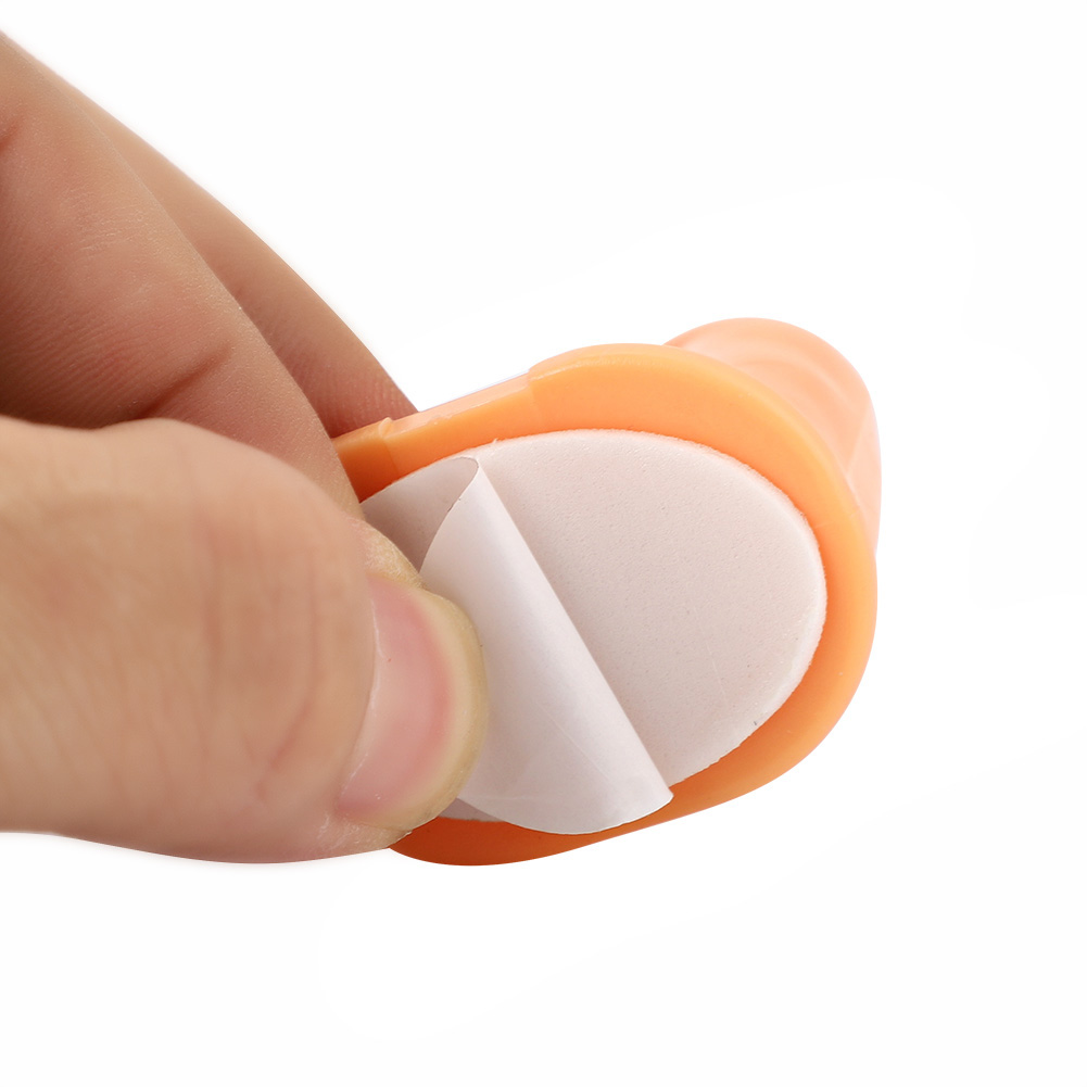 Eine Hand, die ein kleines, orangefarbenes Kunststoffteil mit Klebeband hält.