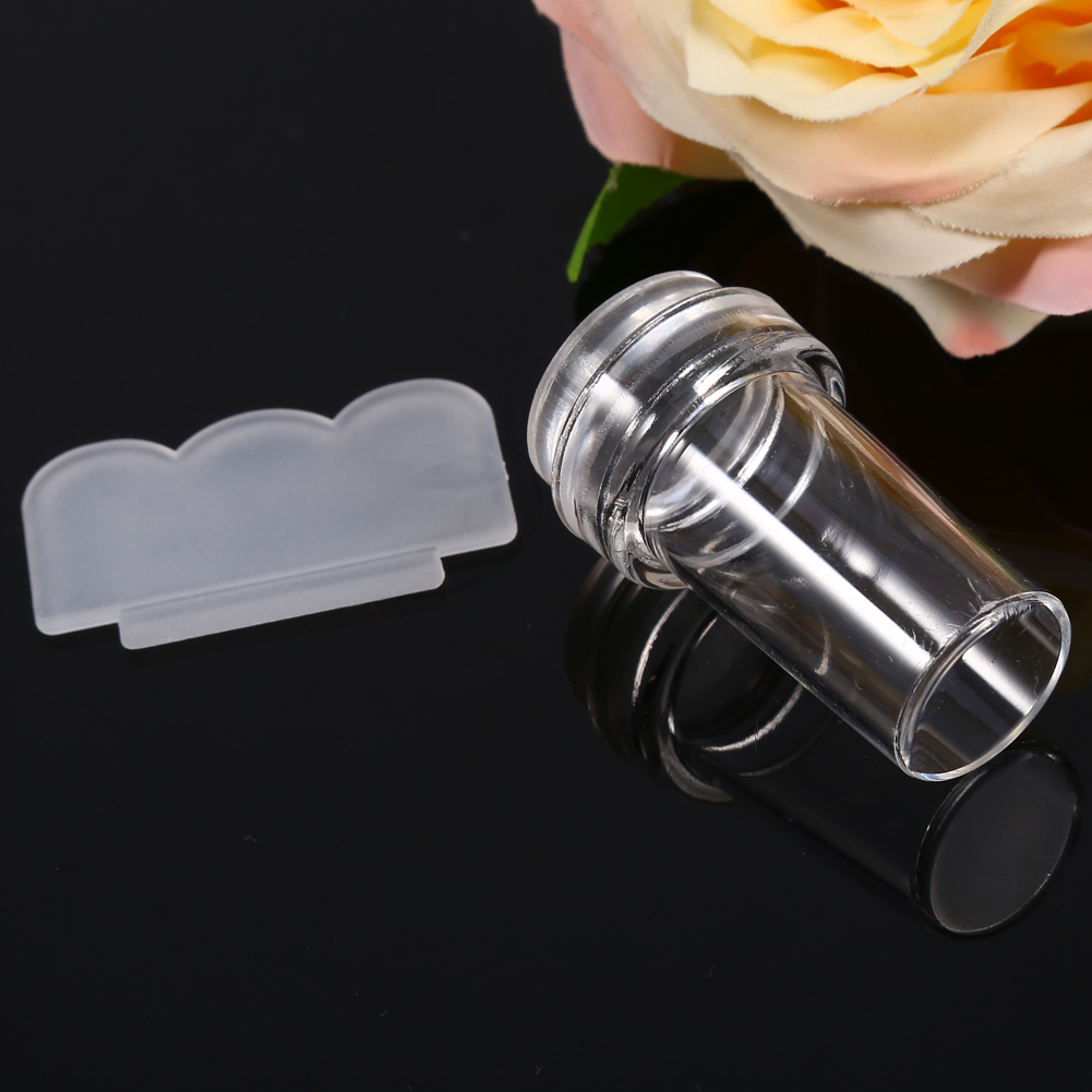 Eine durchsichtige Nagellackflasche mit einem transparenten Applikator und einem transparenten Kunststoffschaber, neben einer rosa Blume.