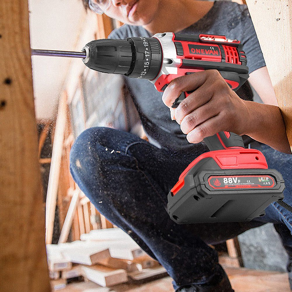 Person bohrt mit einem rot-schwarzen Elektrowerkzeug in Holz. Der Bohrer dringt in das Holz ein.