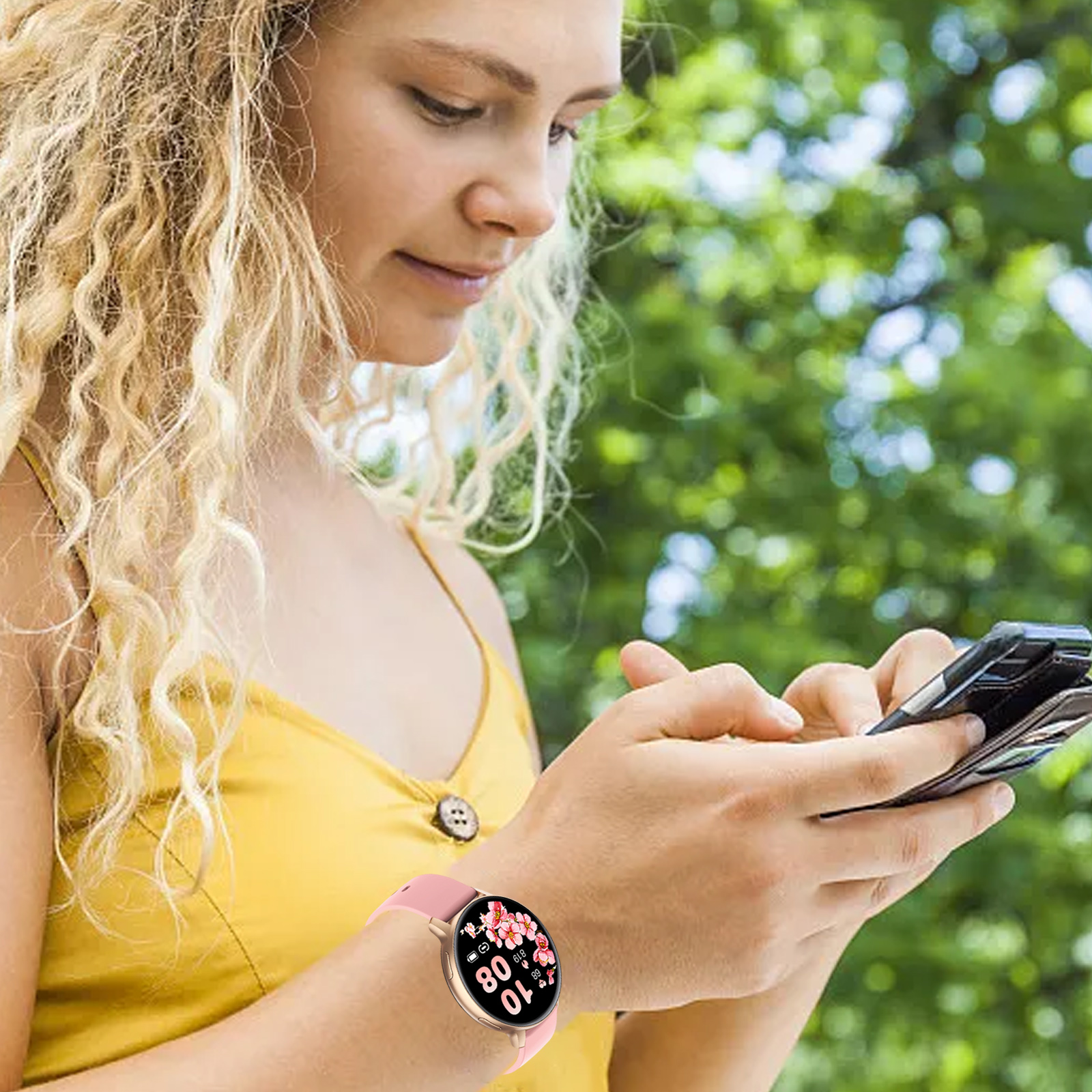 Eine blonde Frau in einem gelben Oberteil schaut auf ihr Telefon. Sie trägt eine Smartwatch mit rosa Armband.