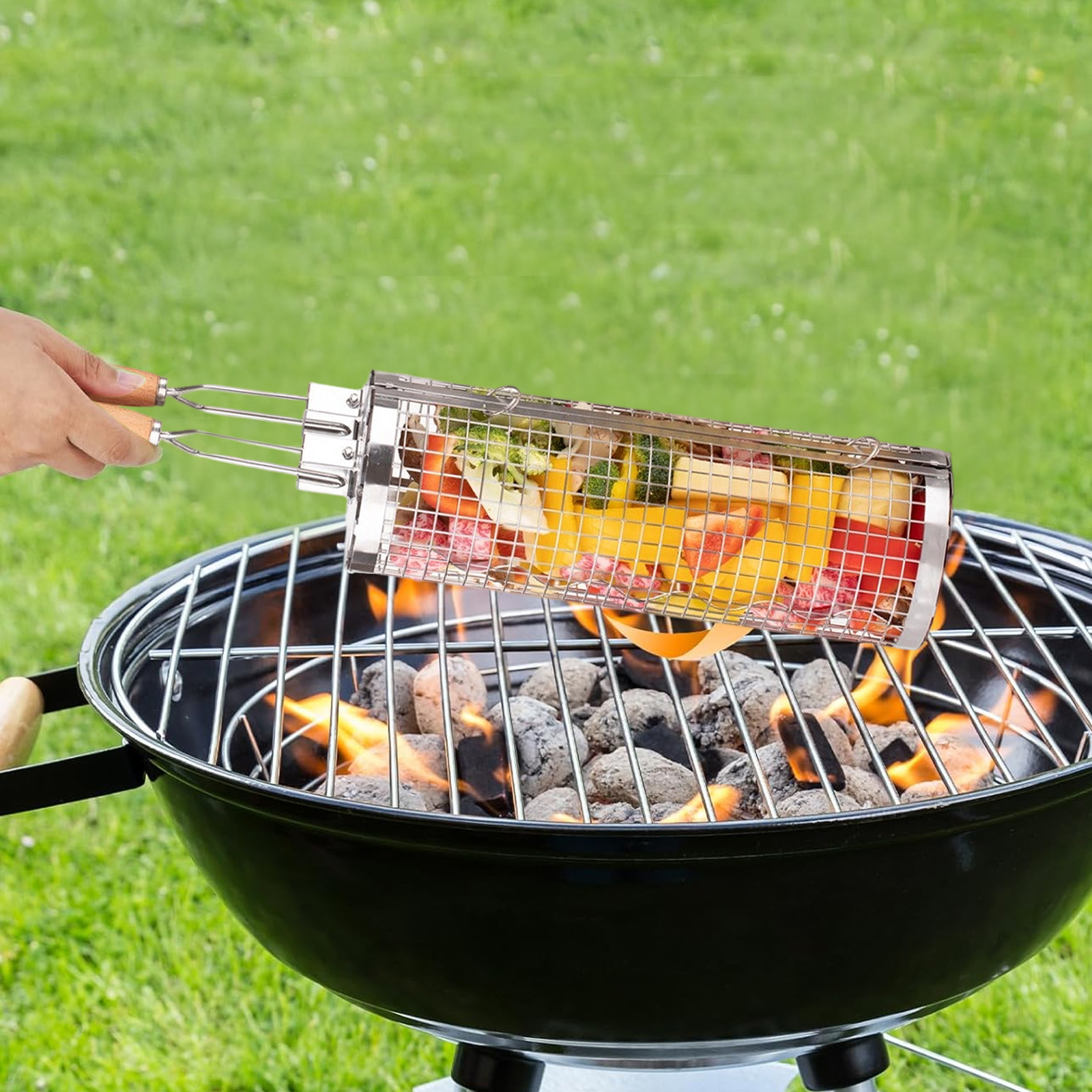 Eine Person grillt Gemüse in einem zylindrischen Metallkorb über einem Holzkohlegrill im Freien.