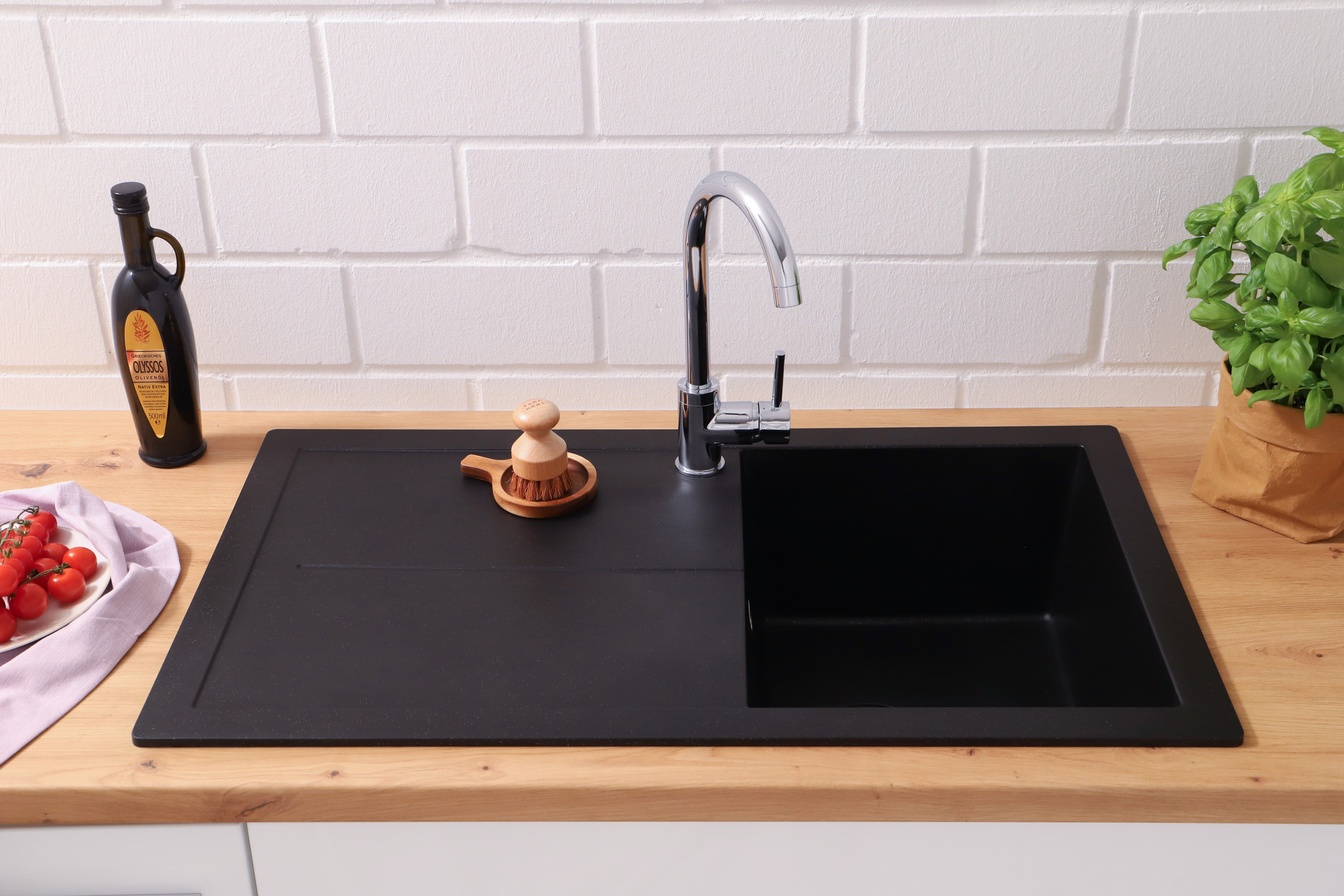 Schwarzes Waschbecken mit Wasserhahn. Rote Tomaten und eine Holzbürste sind sichtbar.