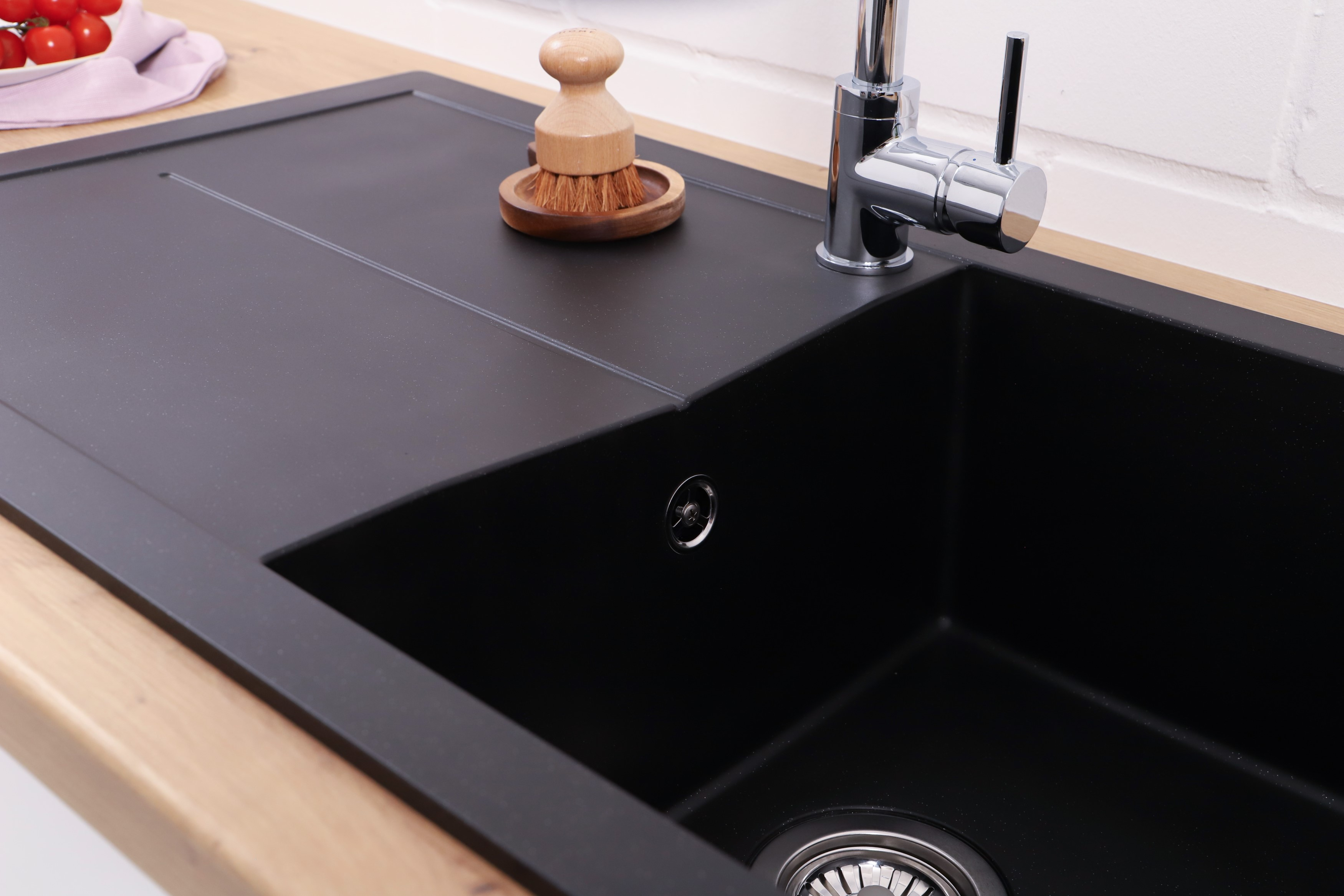 Ein schwarzes Waschbecken mit Wasserhahn und einer Holzbürste auf einer Holz-Arbeitsplatte.