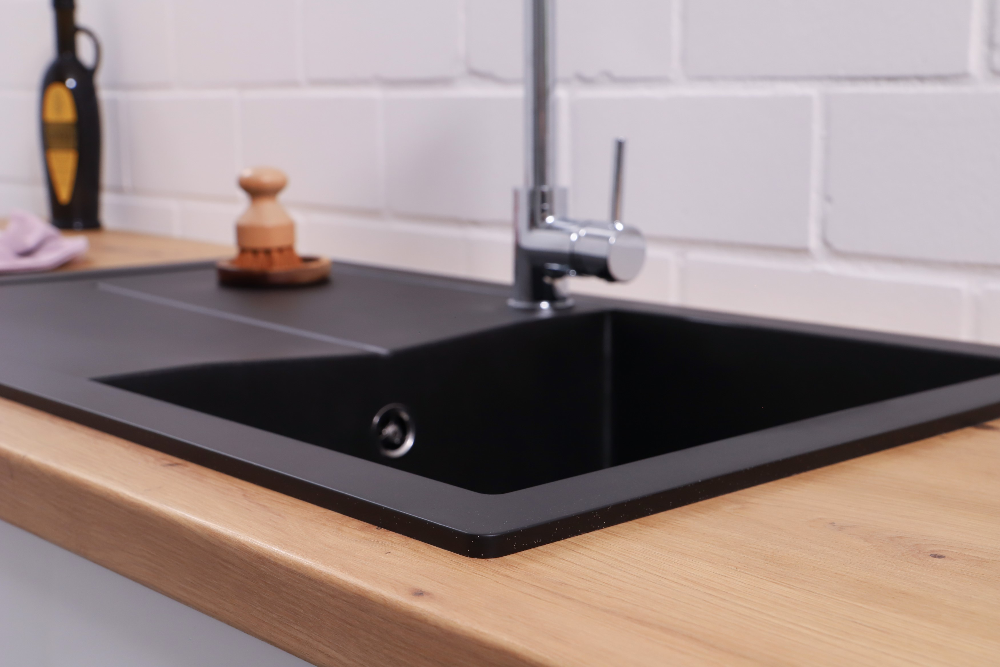 Schwarzes Waschbecken und Wasserhahn auf einer Holz-Arbeitsplatte mit Bürste und Pflanze.