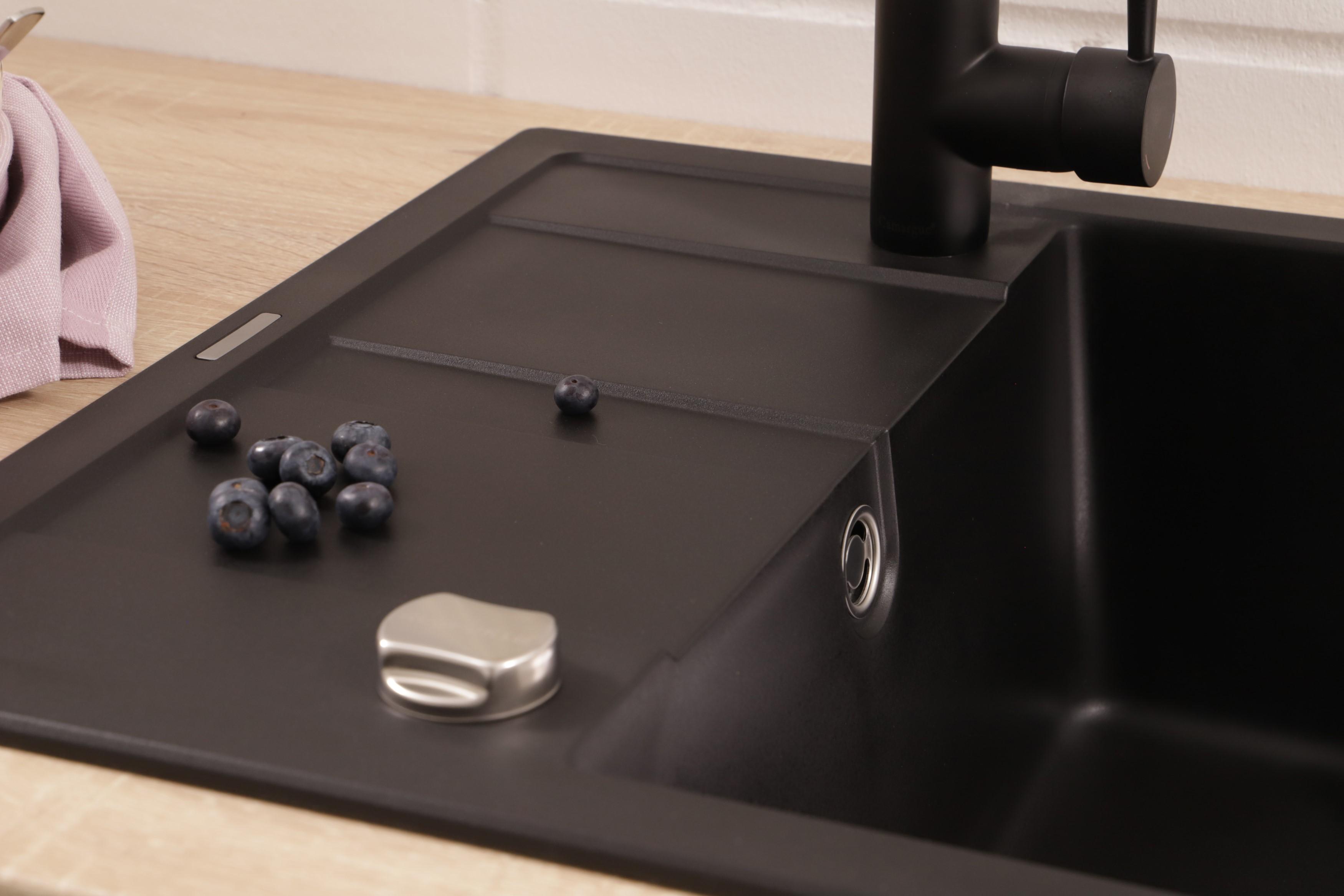 Lavello nero con mirtilli e coperchio in metallo. Superficie in legno chiaro.