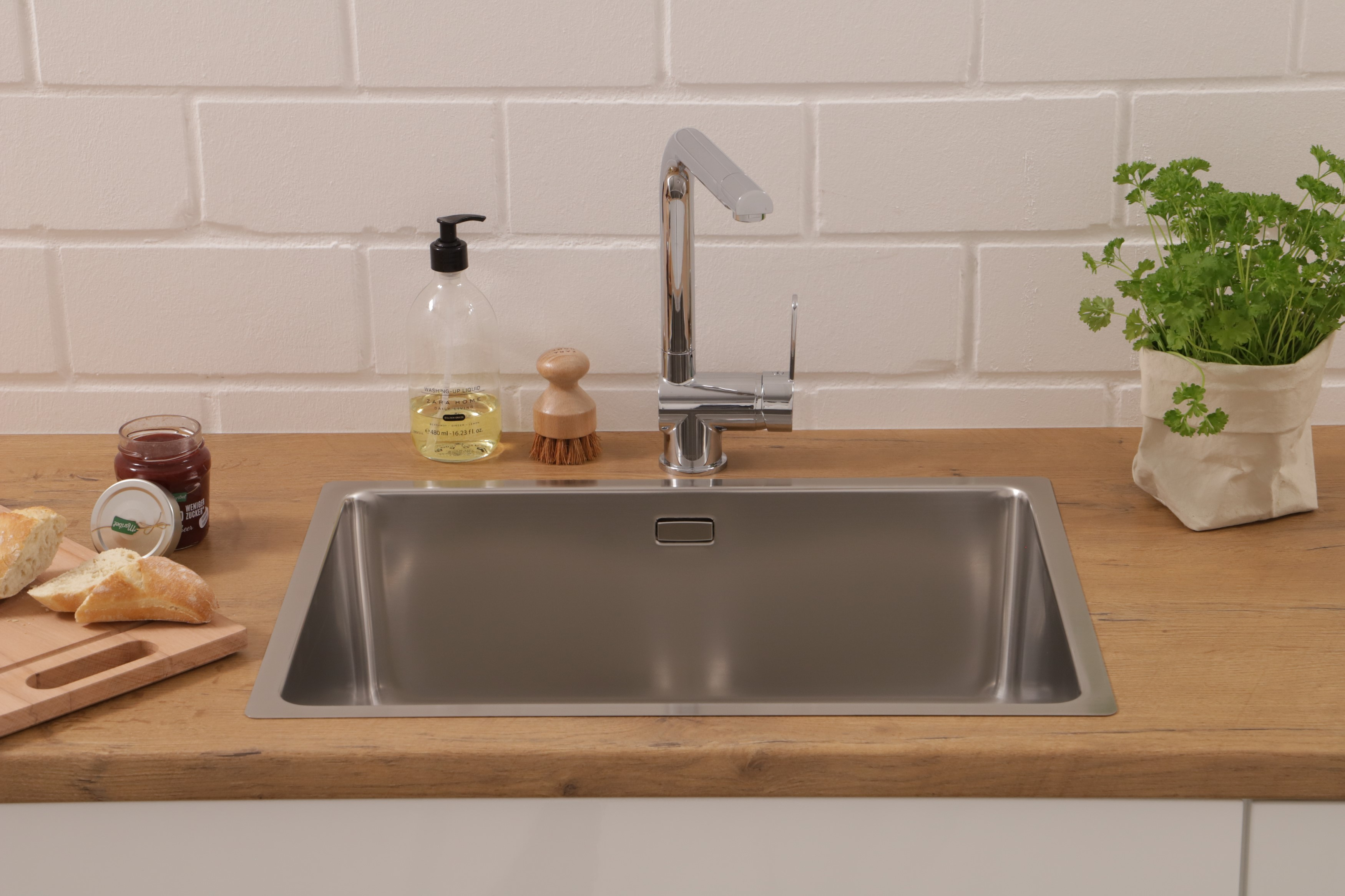 Edelstahlspüle mit Wasserhahn, Seife und Brot. Holz-Arbeitsplatte, weißer Hintergrund.