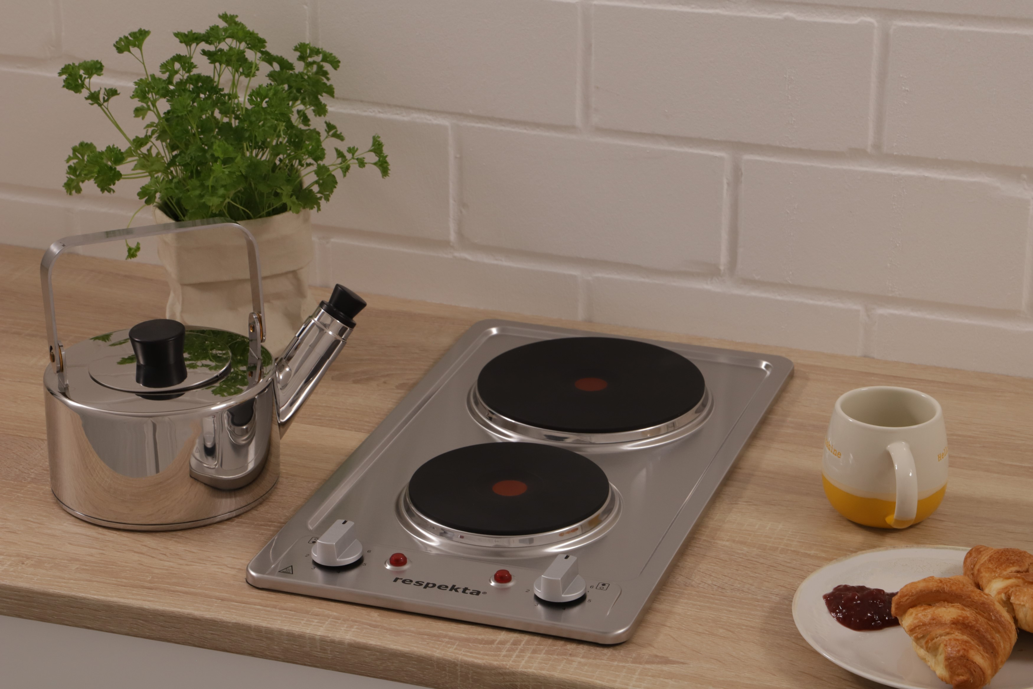 Keuken met een kookplaat, een theepot, een mok, een plant en gebakjes op een houten aanrecht.