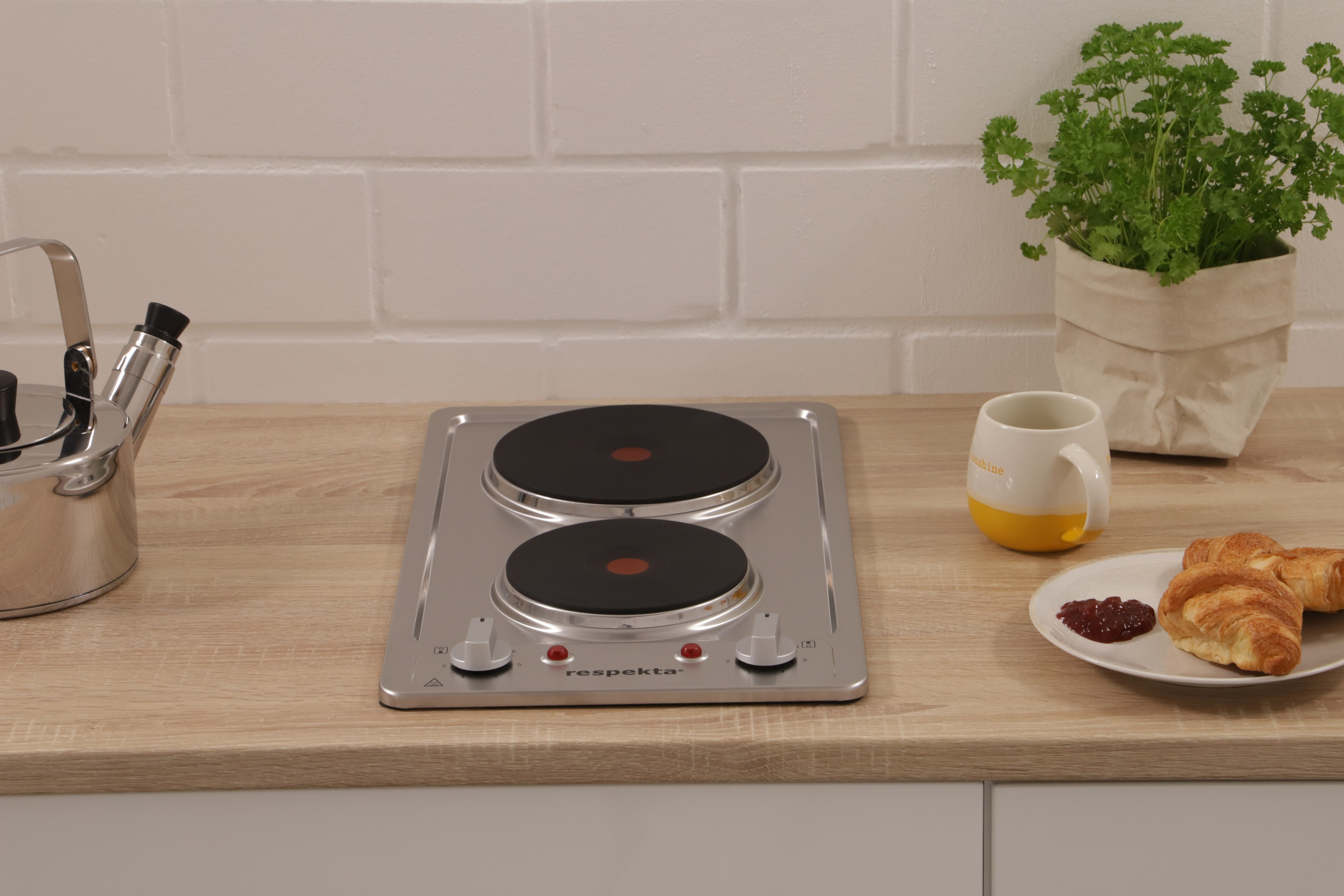 Keuken met een kookplaat, een theepot, een mok, een plant en gebakjes op een houten aanrecht.