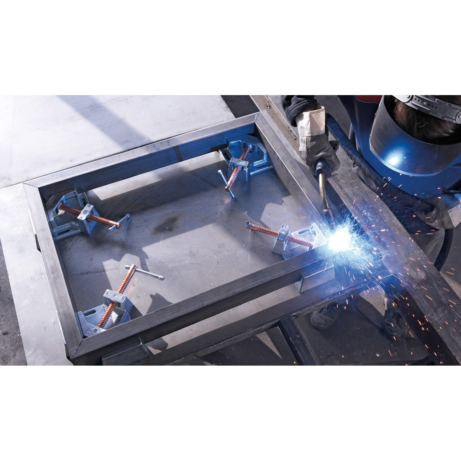 Ein Schweißer arbeitet an einem Metallrahmen, mit Klemmen, die die Ecken sichern.