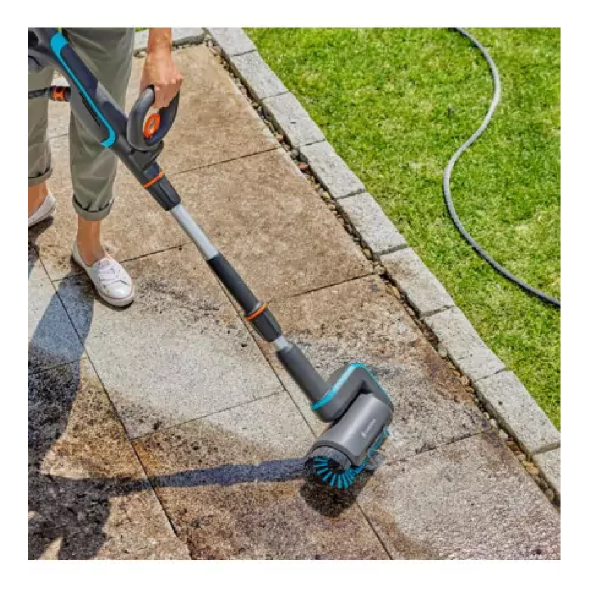 Una persona che usa una spazzola per la pulizia su un patio. La testina è rotonda, blu e nera. Il patio è grigio.