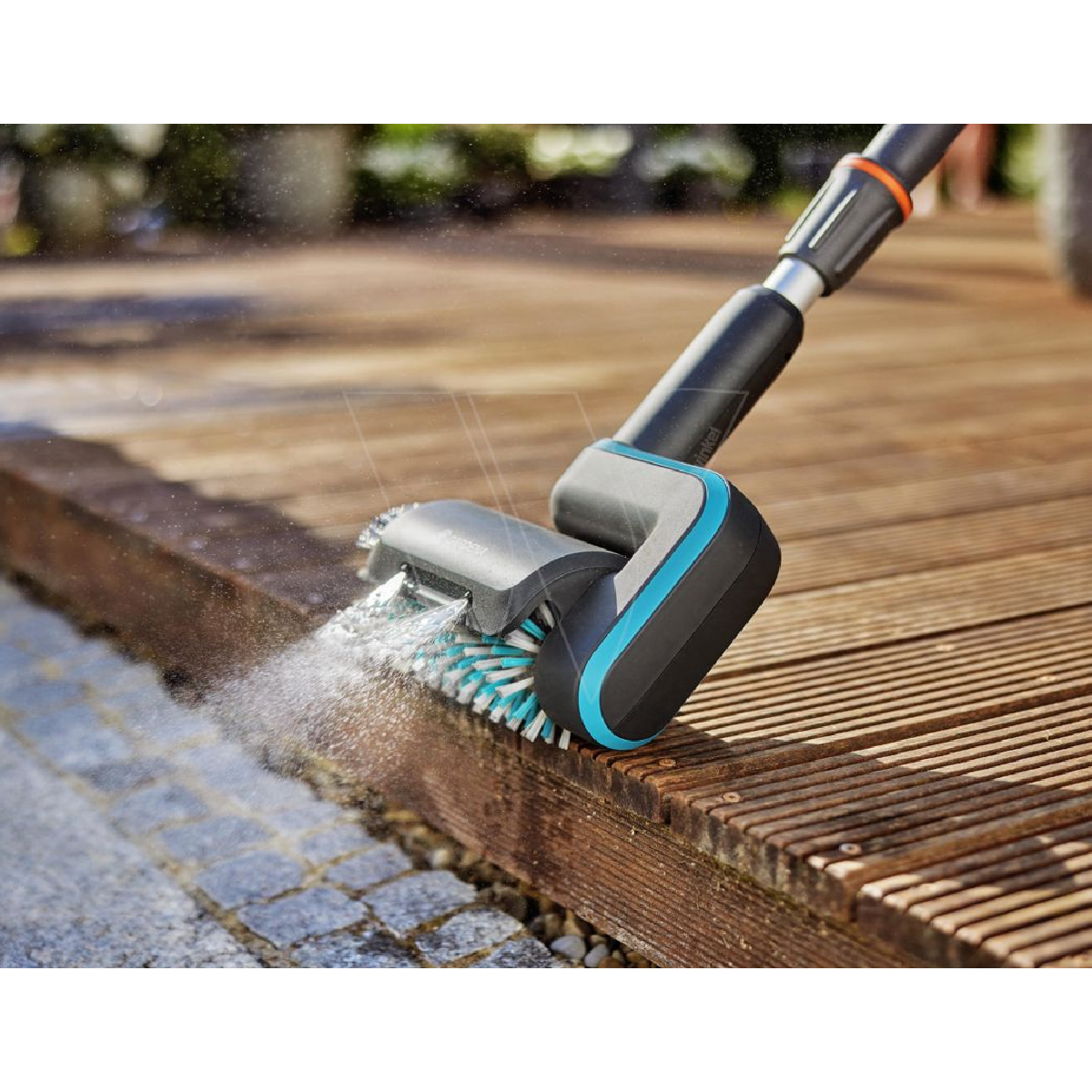 Una spazzola per la pulizia che spruzza acqua su un'area di legno. La testina è blu e nera. Lo sfondo è sfocato.