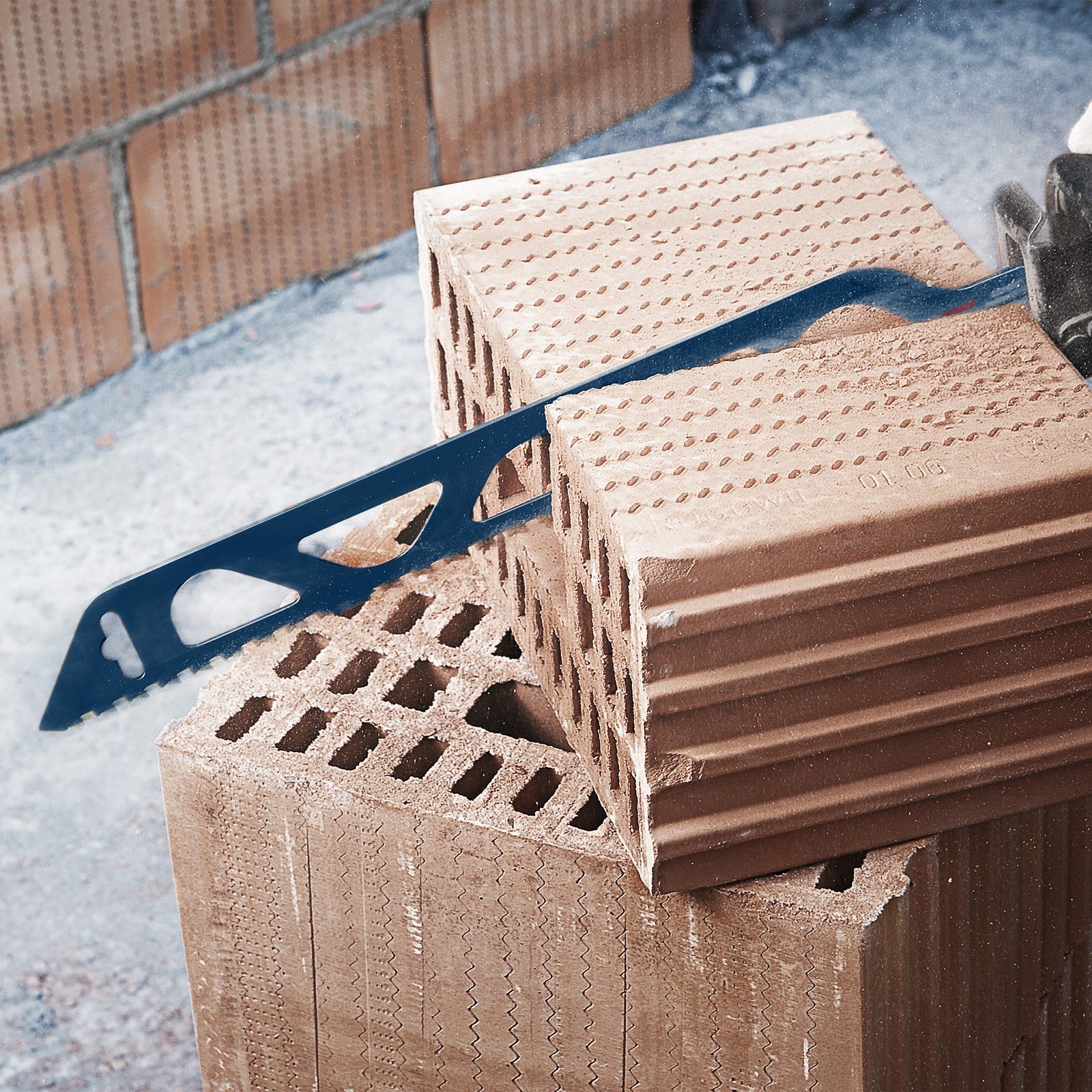 Piła tnąca przez cegły. Piła jest niebieska, a cegły brązowe. Piła jest w akcji.